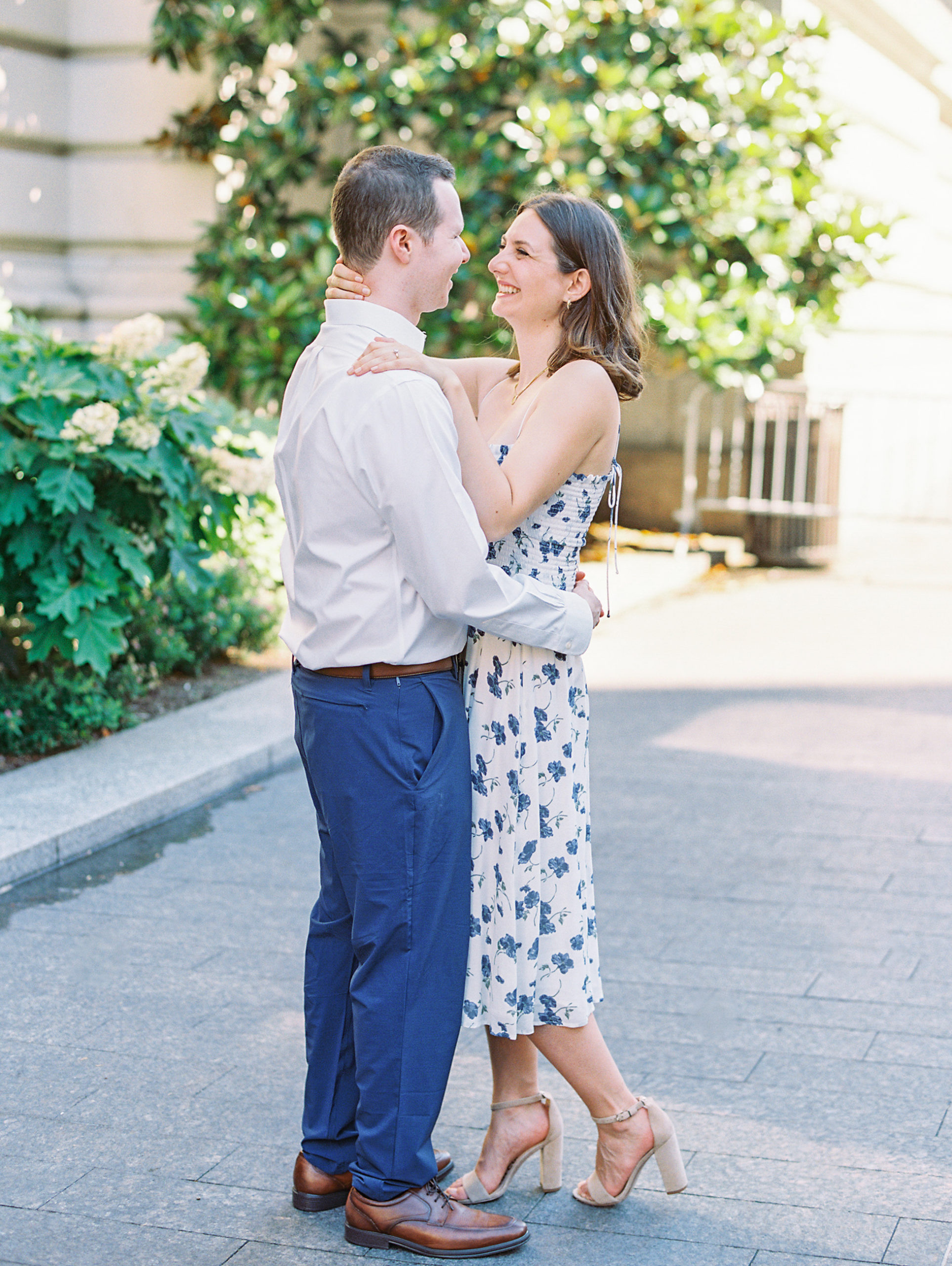 Couple embraces and laughs on pathway with white hydrangeas and trees