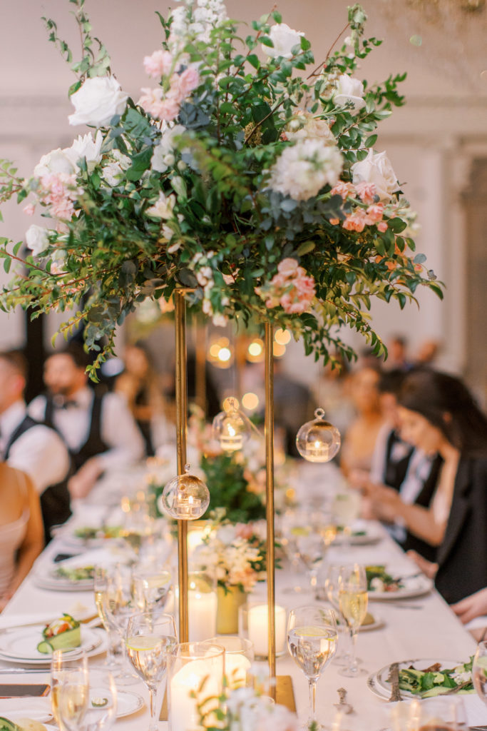 Rose centerpiece at wedding reception with hanging candles and gold details 