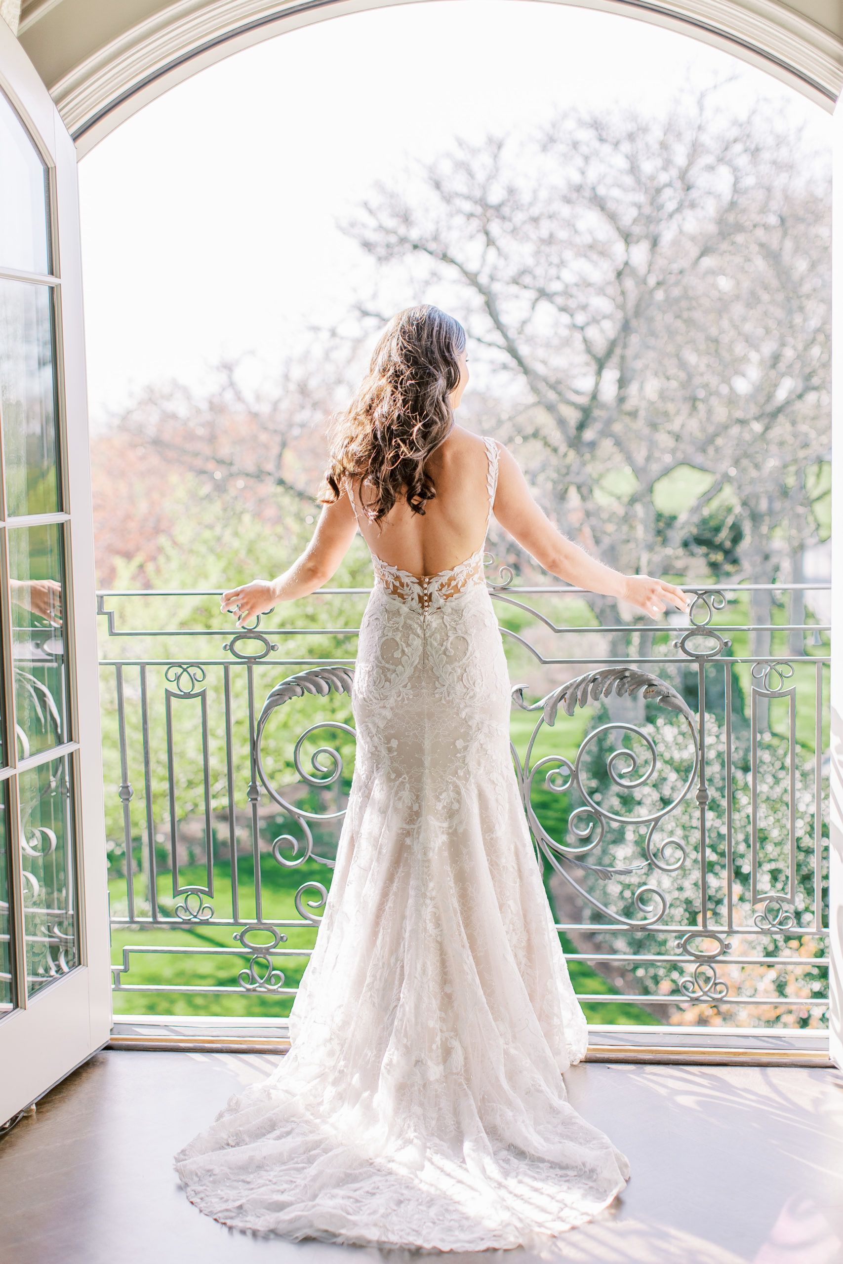 Bride looking out on balcony with wedding dress flowing behind 