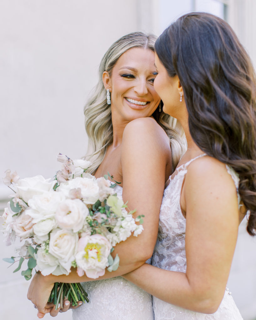 Brides smile and embrace holding rose bouquets 