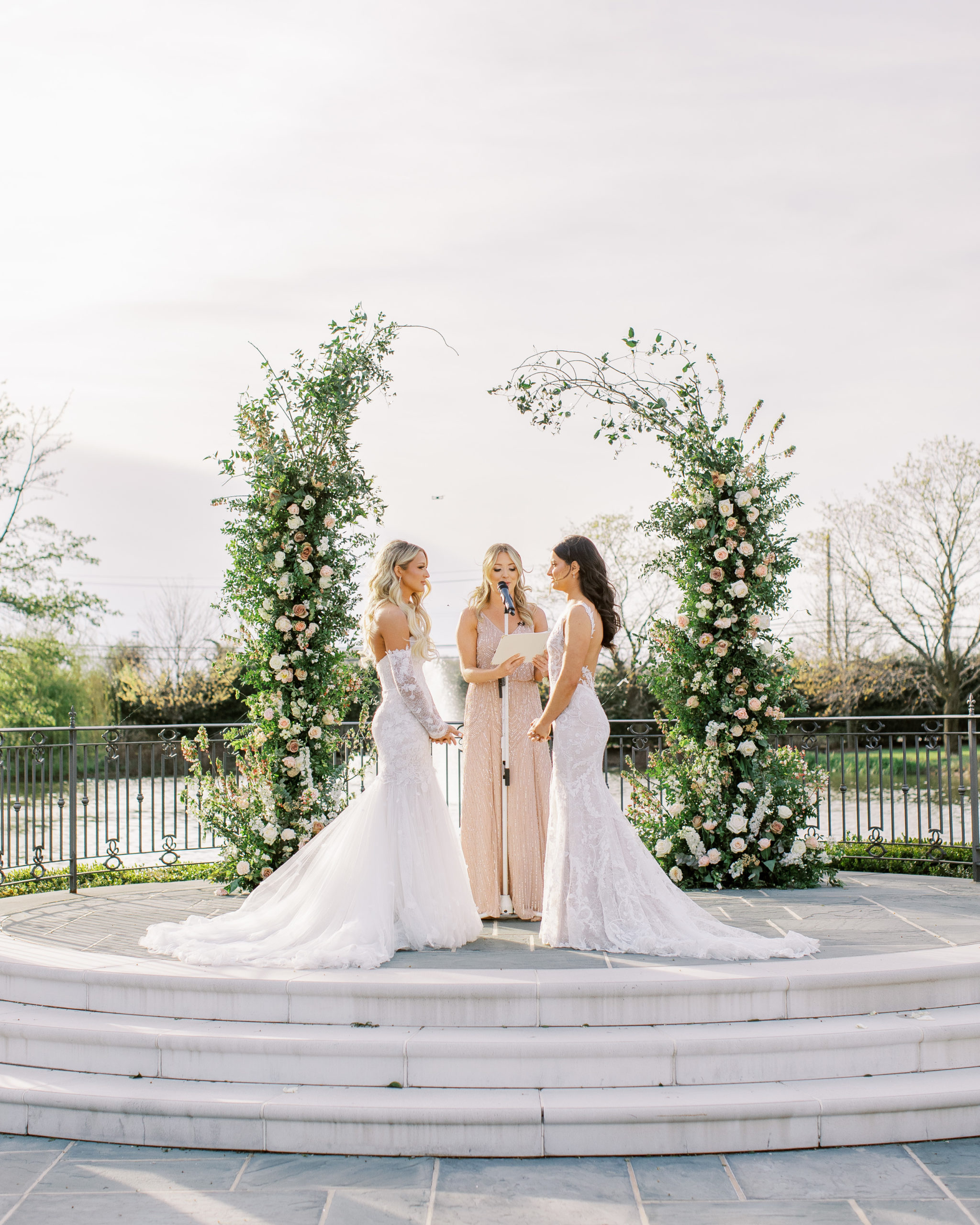 Brides under white and peach rose arch at wedding ceremony for a Romantic Park Chateau Wedding Photography