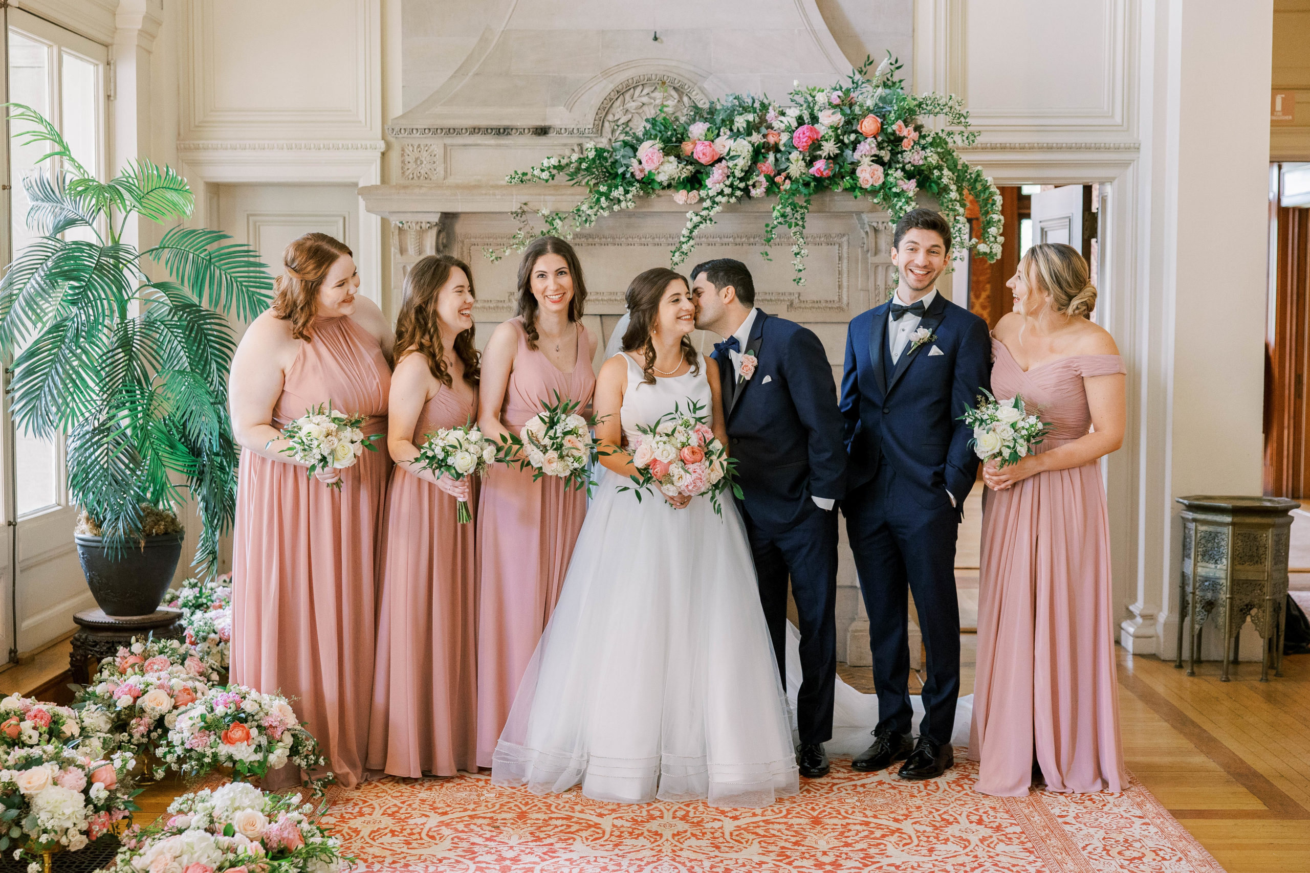 Groom kisses bride on cheek with bridal party smiling and laughing at Cairnwood Estate Wedding Photography