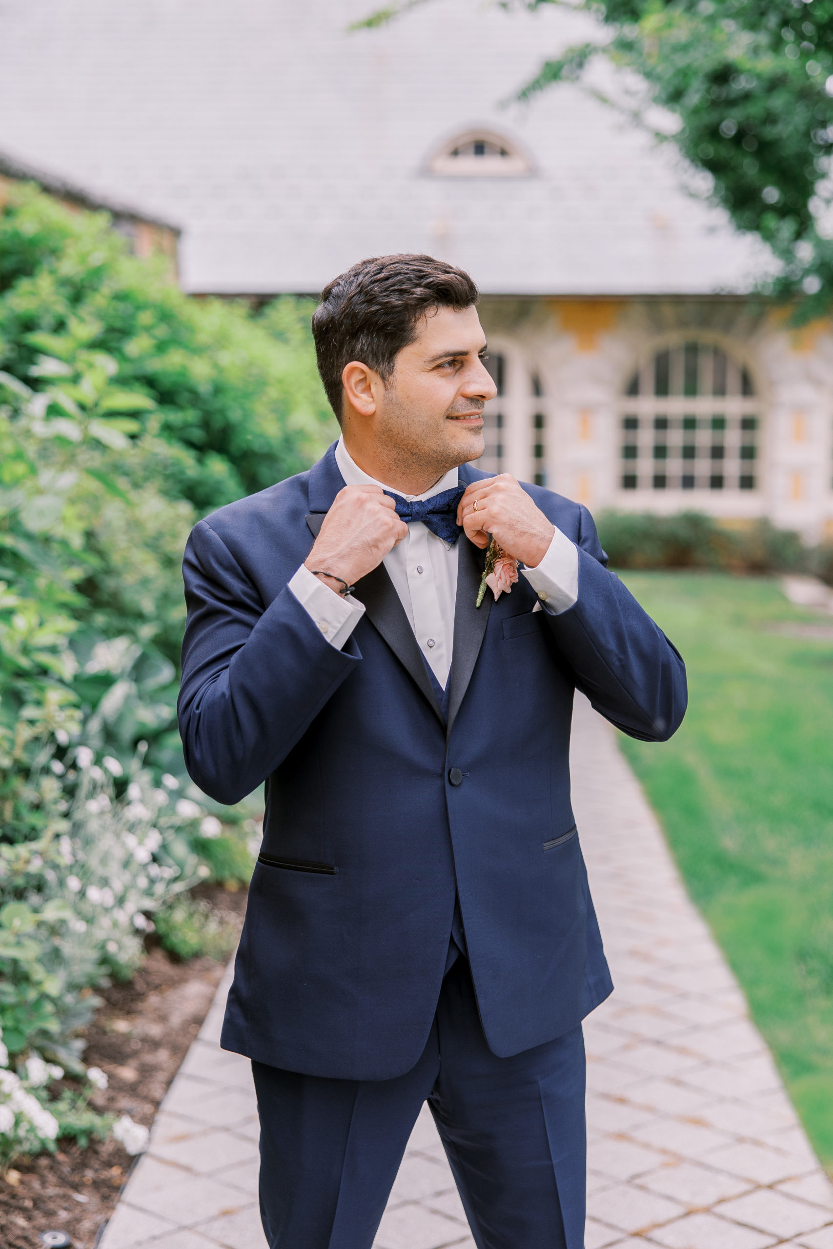 Groom adjusts his tie wearing a navy suit in garden for Cairnwood Estate Wedding Photography