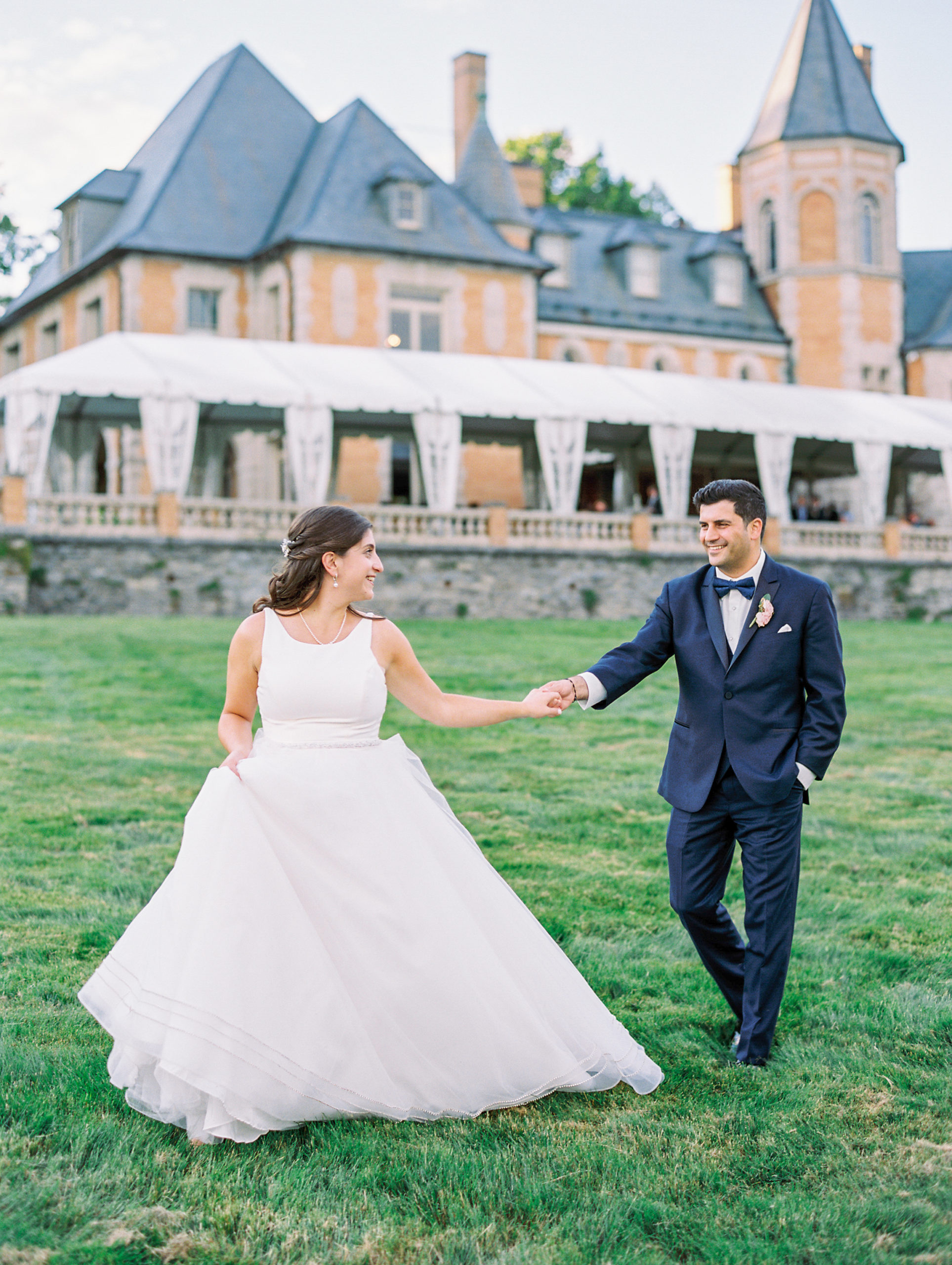 Bride and groom hold hands walking in front of limestone and brick chateau inspired estate for Cairnwood Estate Wedding Photography