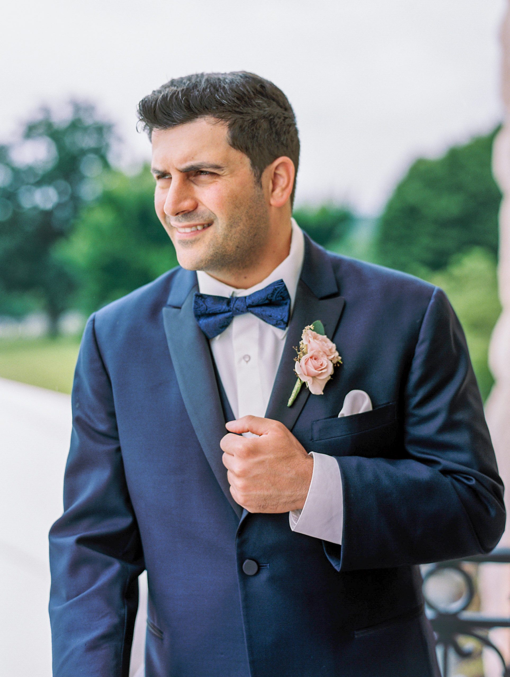 Groom poses away in navy suit with pink rose corsage and blue bow tie 