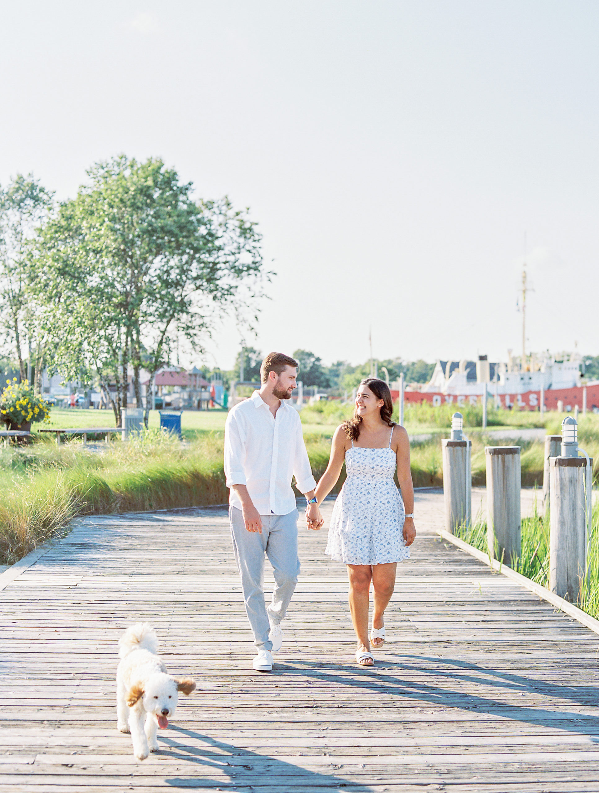 Couple holds hands walking along dock with dog 
