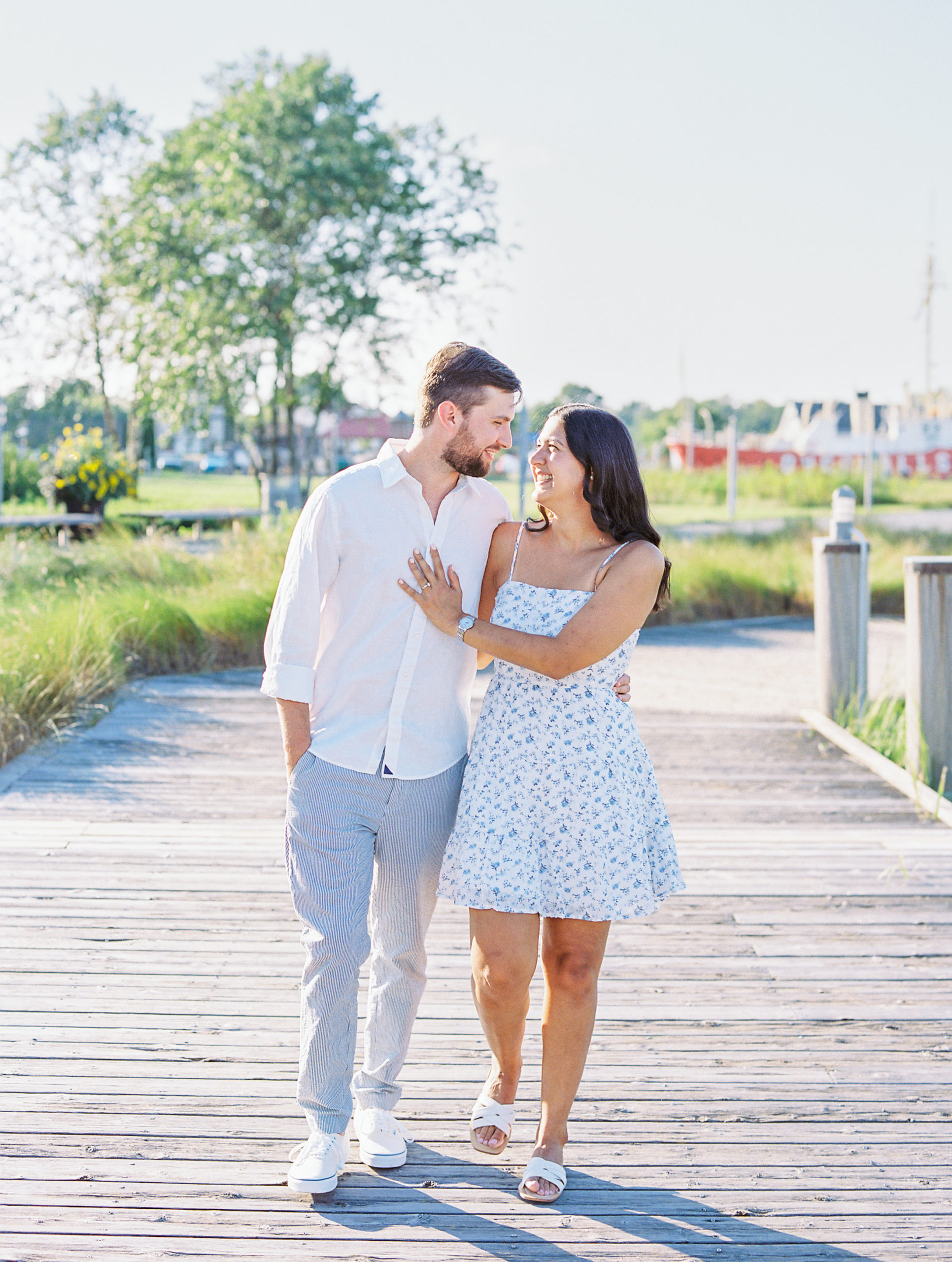 Couple smiles, walks, and laughs on wooden boat dock for Summer Lewes Engagement Session
