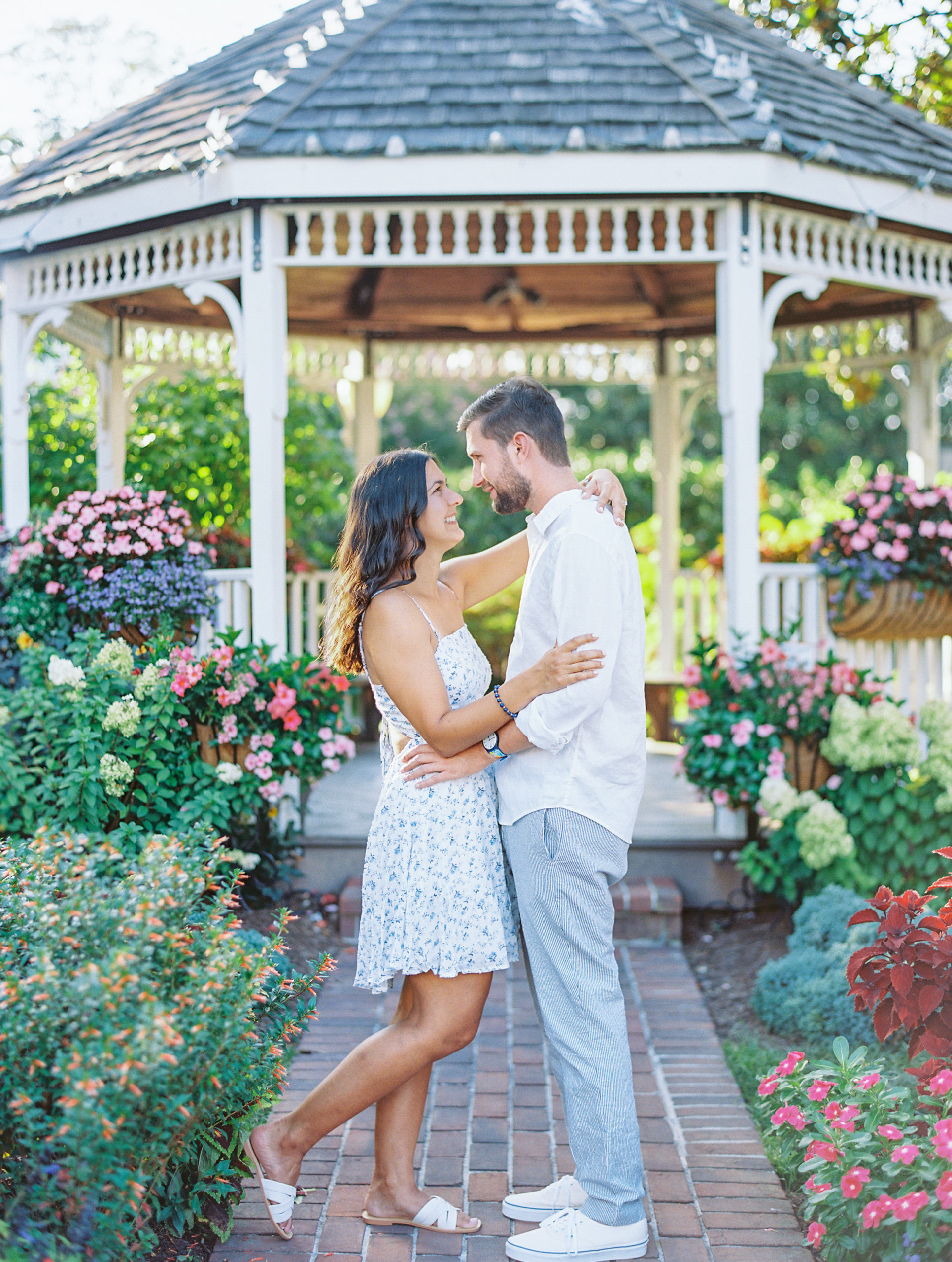 Couple embraces and smiles in front of gazebo garden 