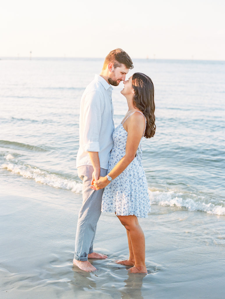 Couple hold hands and lean in for a kiss by the water 