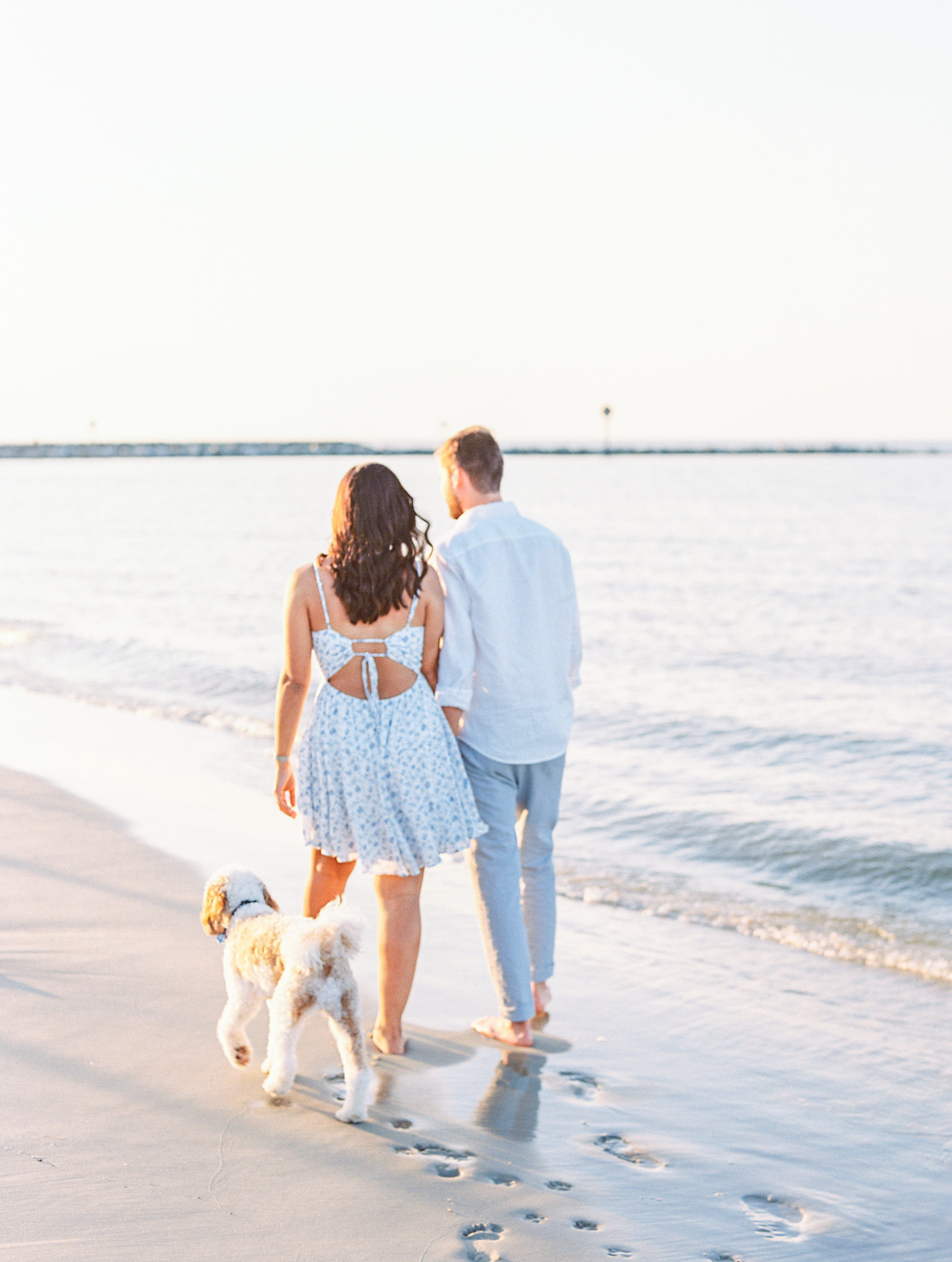 Couple walking along the beach at sunset with their dog