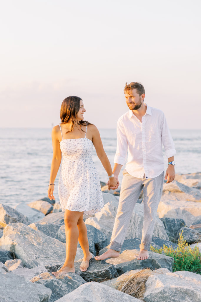 Couple holds hands and smiles walking along jetty for Summer Lewes Engagement Session
