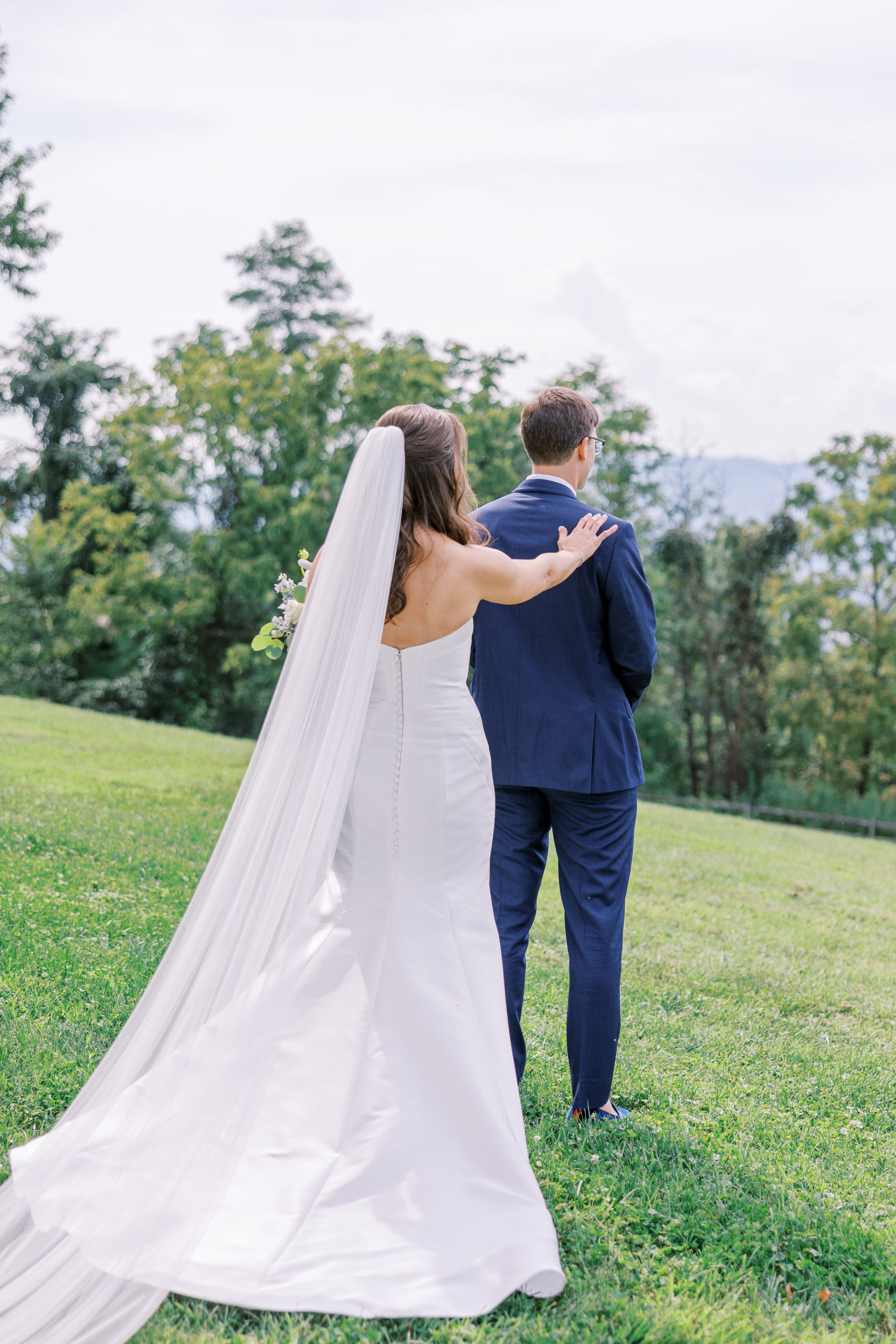 Bride taps grooms shoulder on green mountain landscape for the first look for Charlottesville Wedding Photography

