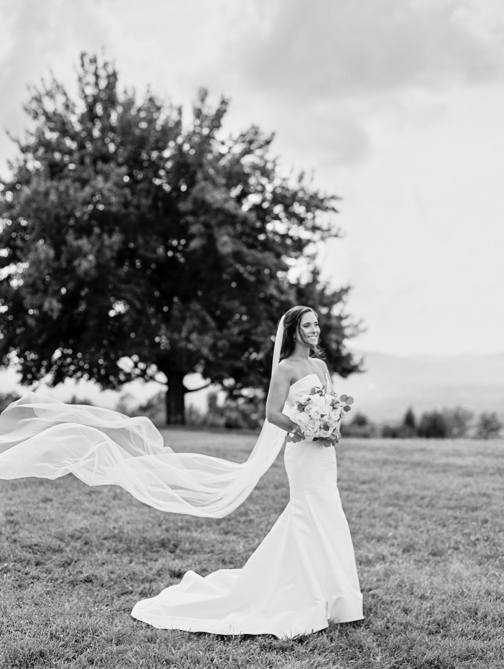 Bride smiles holding rose bouquet as her veil flows in the wind for Charlottesville Wedding Photography
