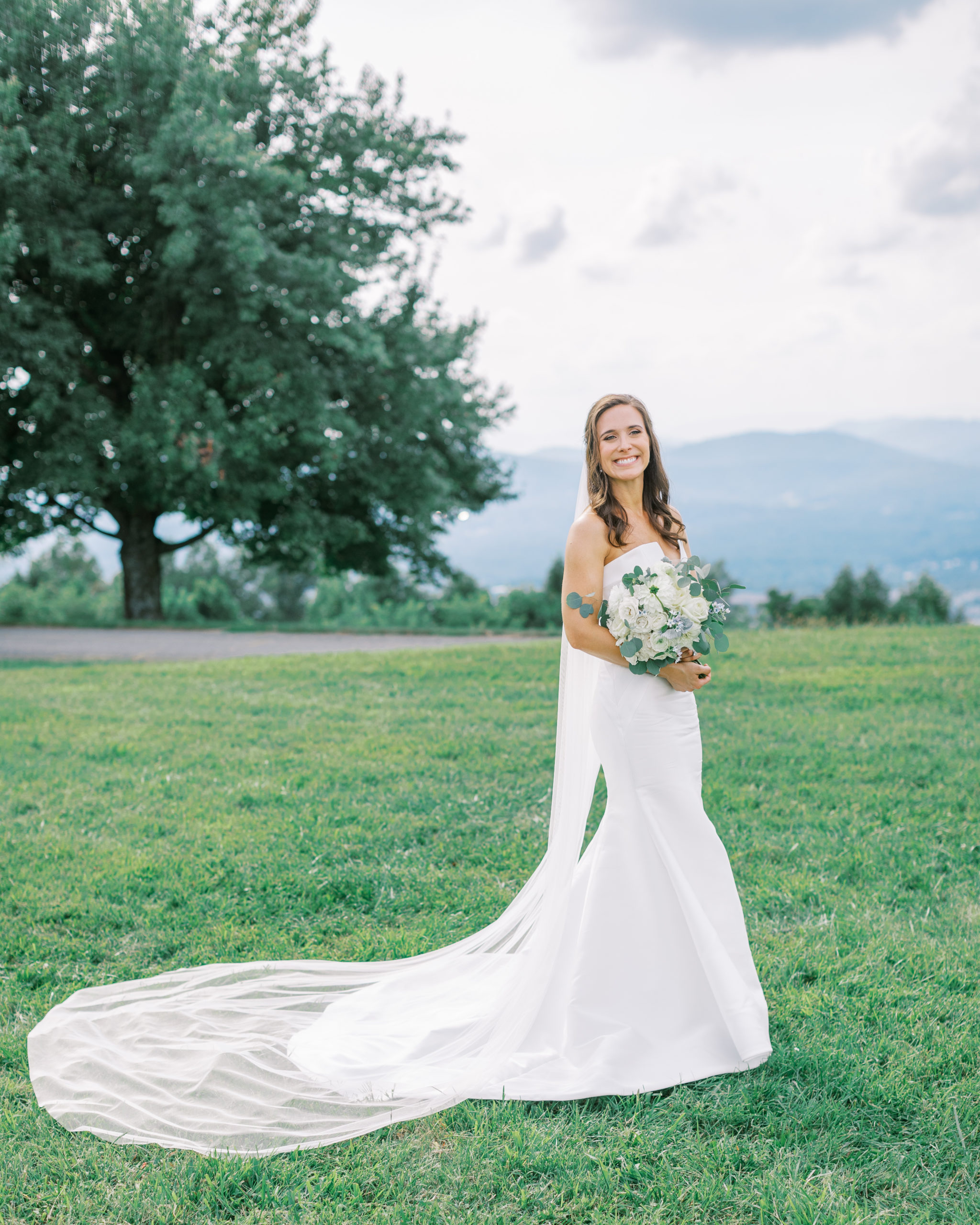 Bride smiles holding her ivory rose bouquet atop mountainside for Charlottesville Wedding Photography
