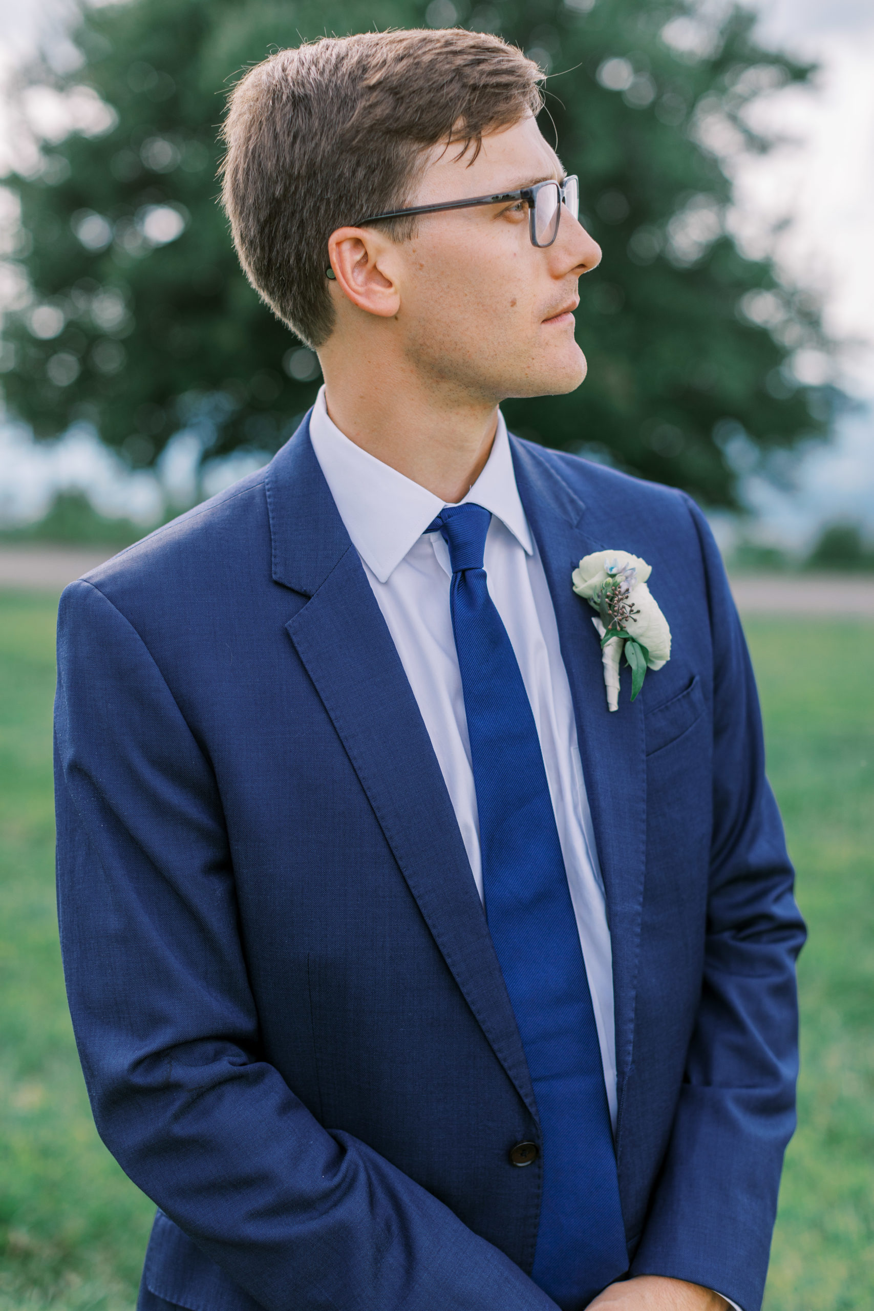 Groom poses and looks away wearing a navy blue suit and blue tie 