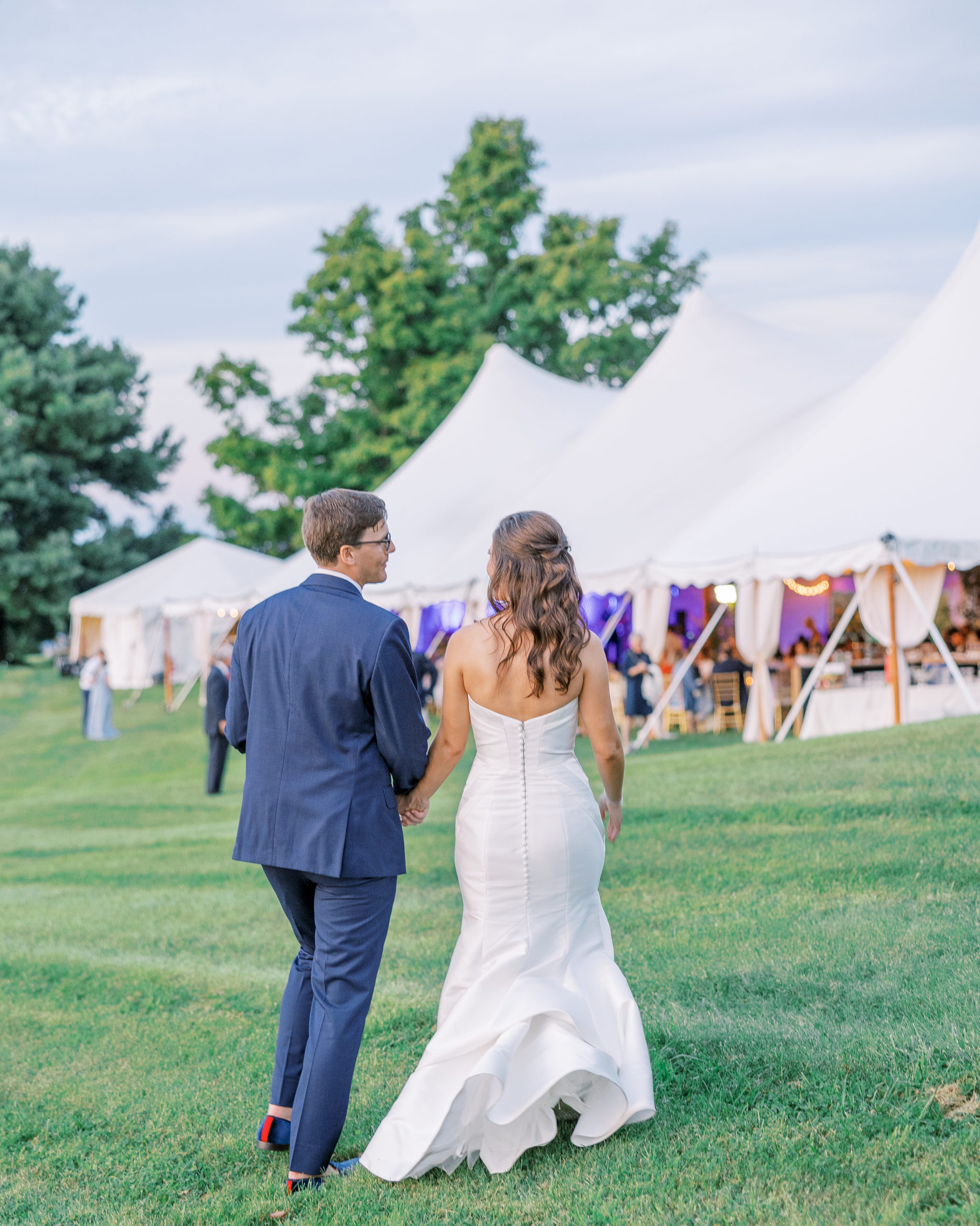 Bride and groom hold hands as they walk towards wedding reception with large white tents for Charlottesville Wedding Photography

