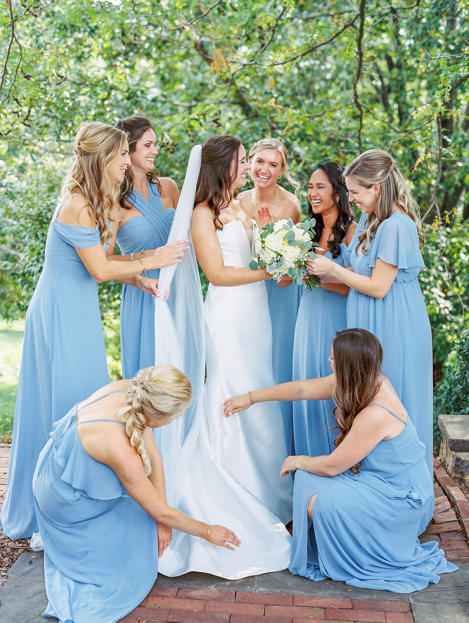 Bridesmaids in light blue dresses around bride laugh and smile 
