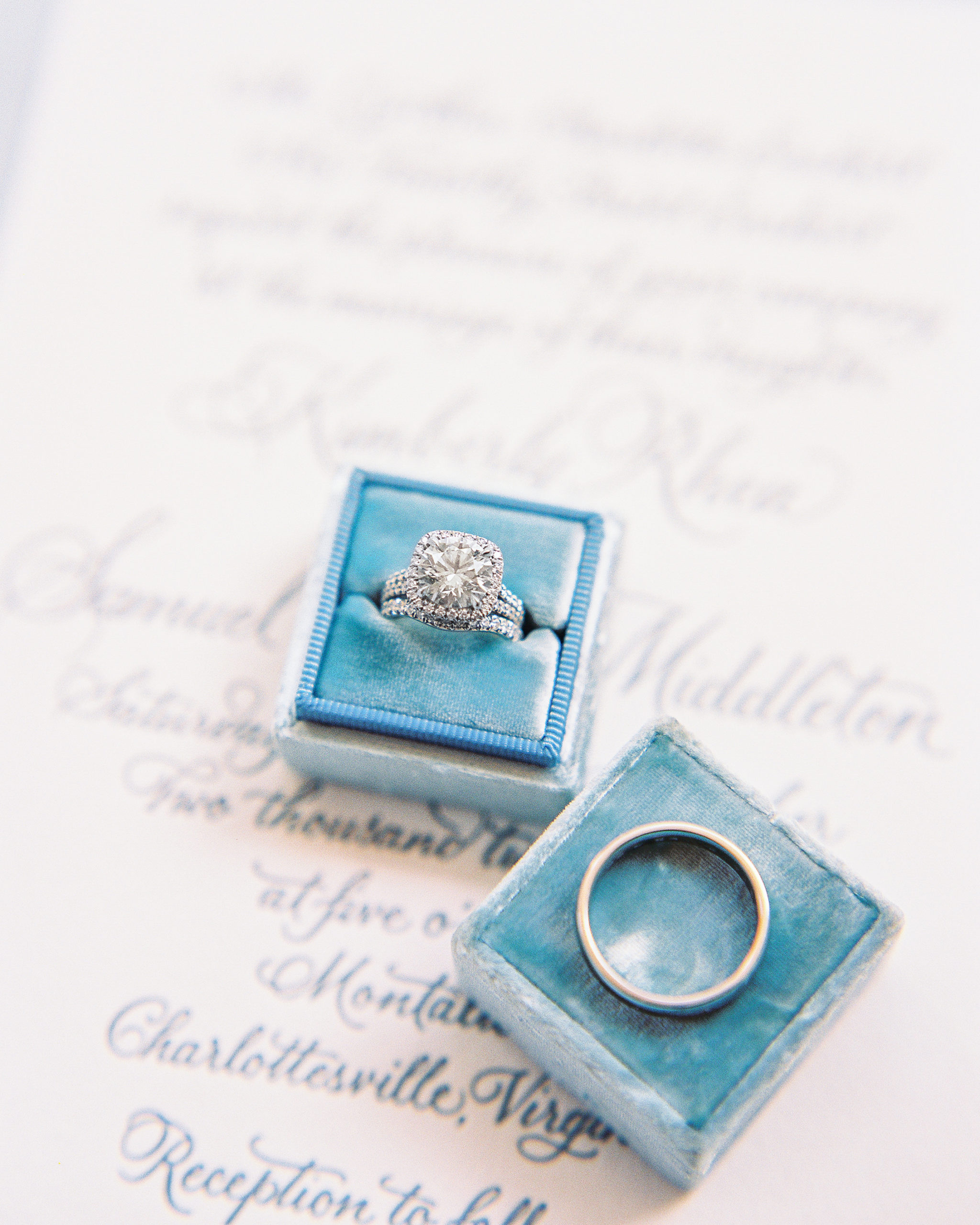 Wedding rings in blue ring box on top of wedding invitation 