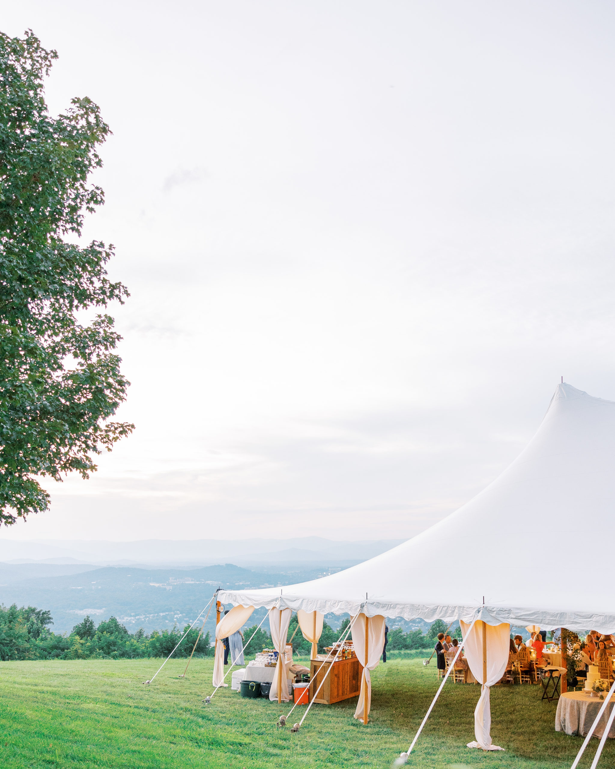 Wedding reception on lawn underneath white tent overlooks the hills 