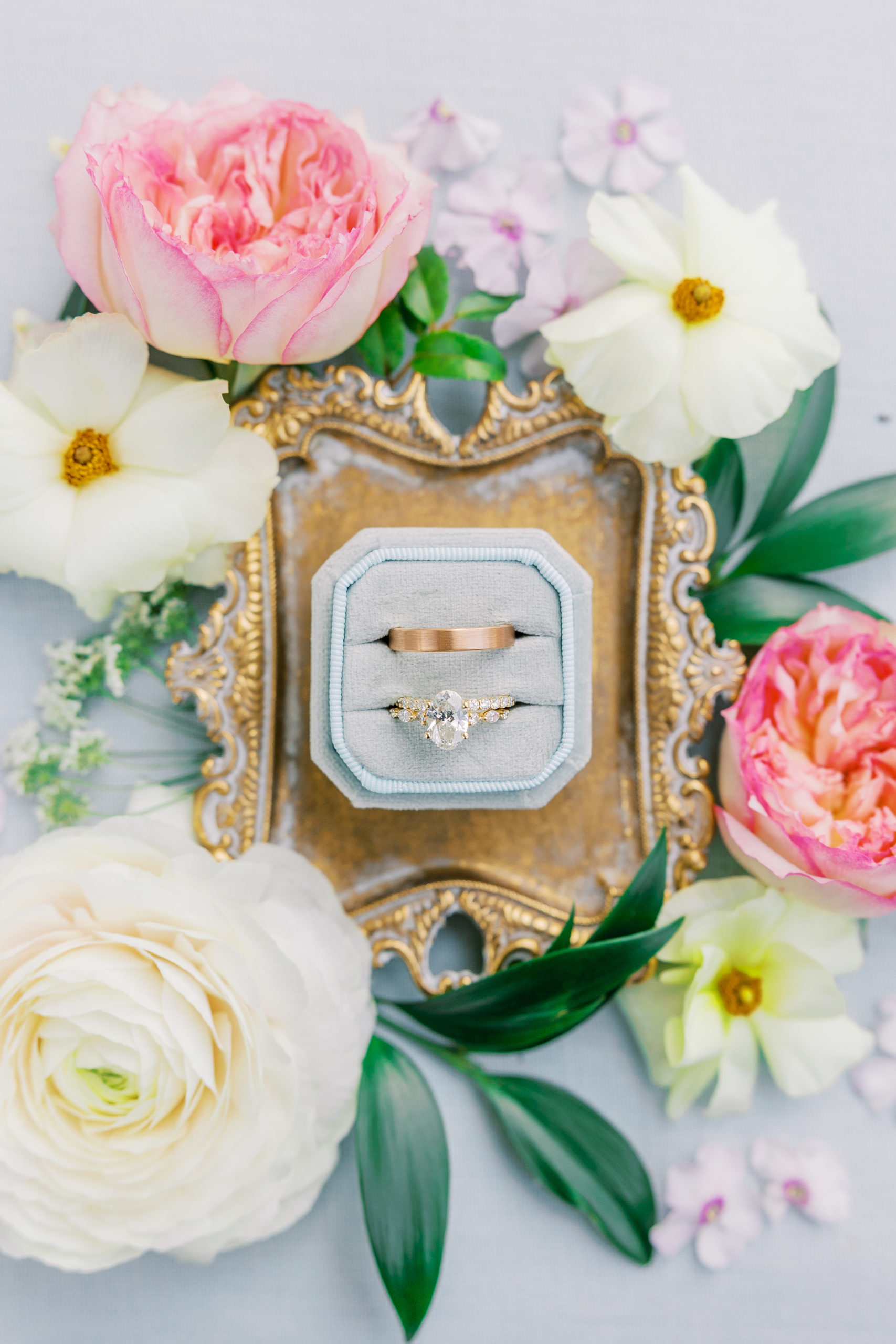 Wedding rings on top of small golden tray with pink and cream flowers