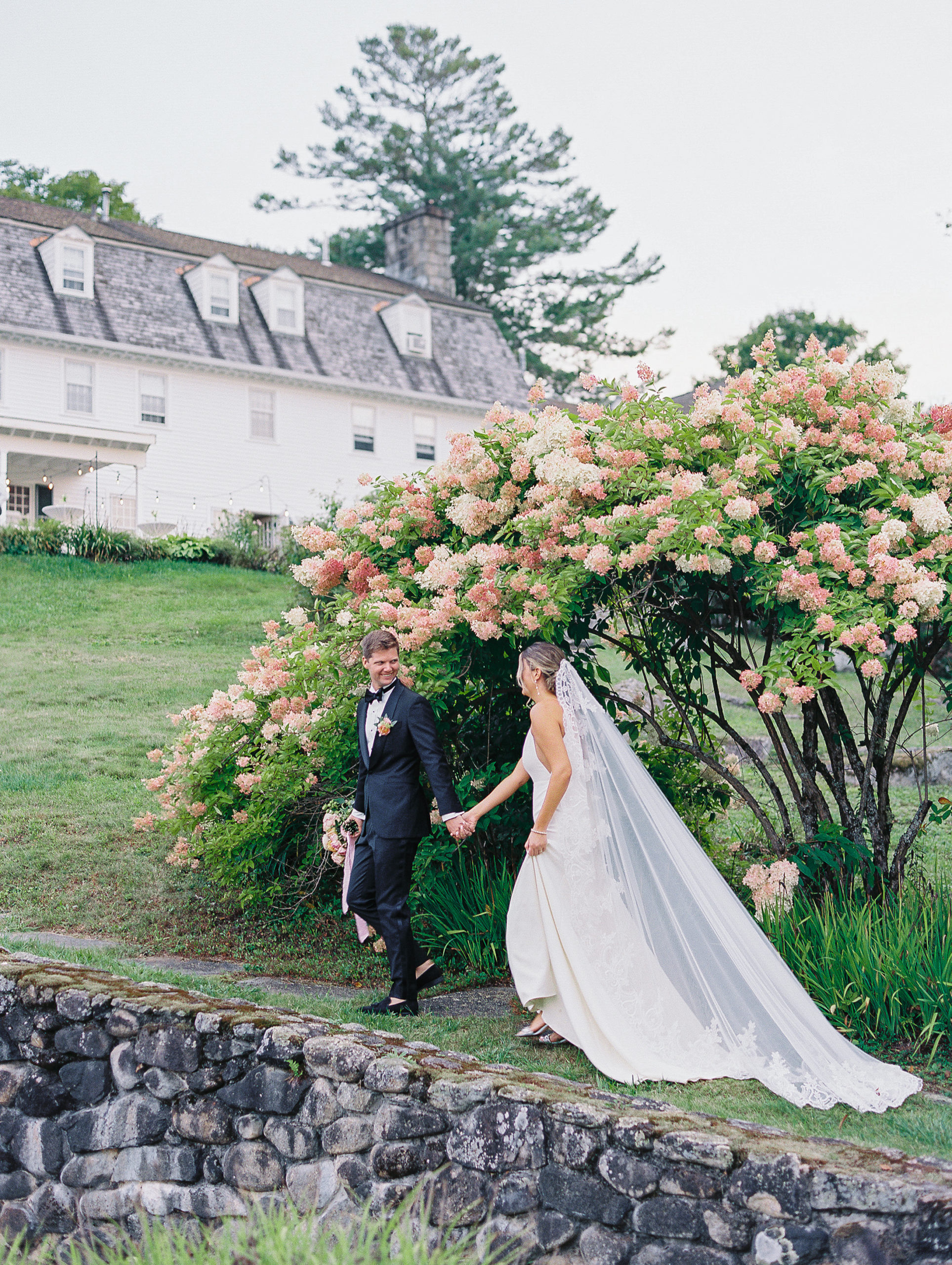 Groom leads bride to reception area underneath pink and cream flower tree for New Hampshire Wedding Photography