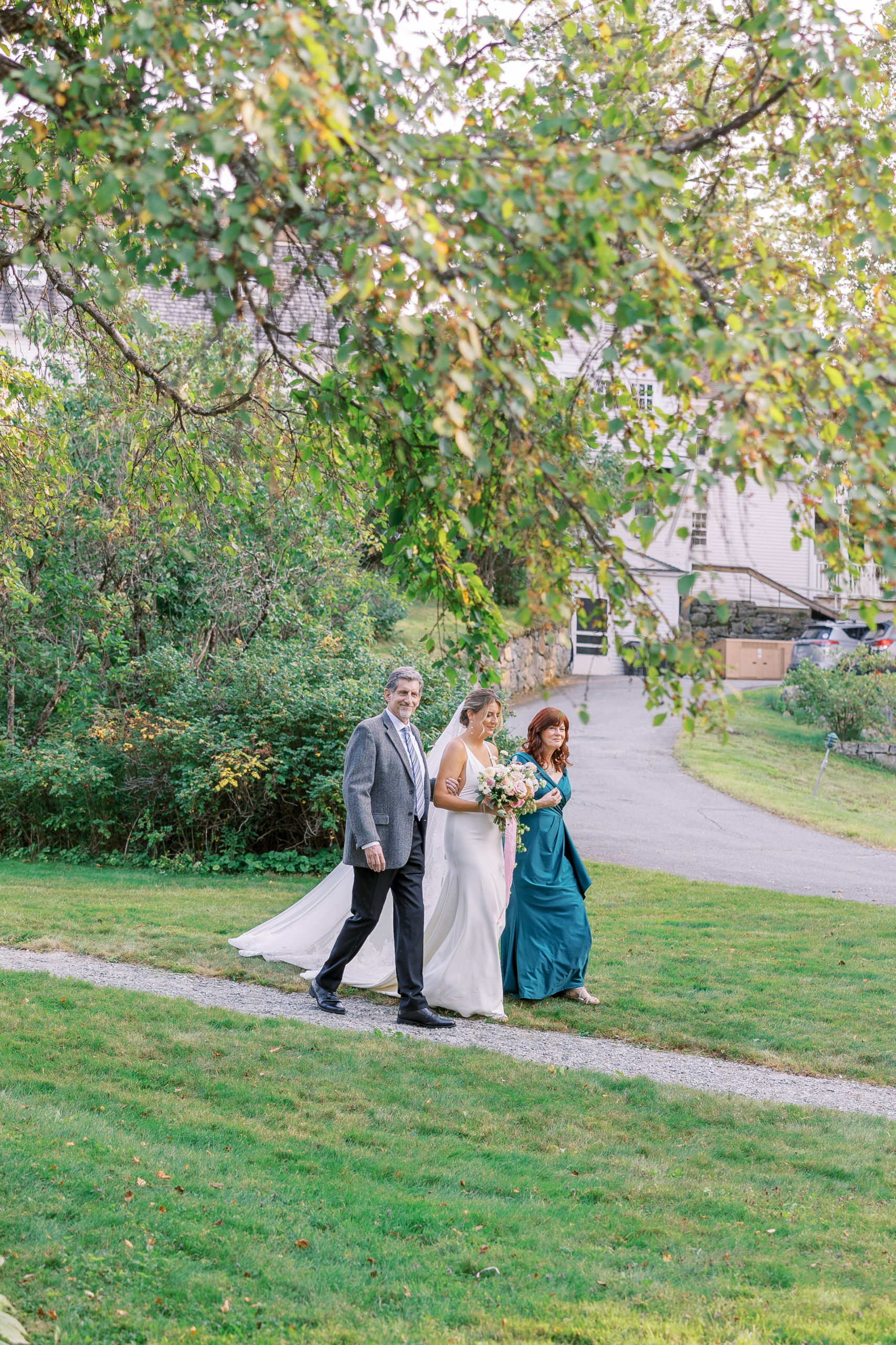 Bride and family walks toward the wedding aisle along gravel path for New Hampshire Wedding Photography
