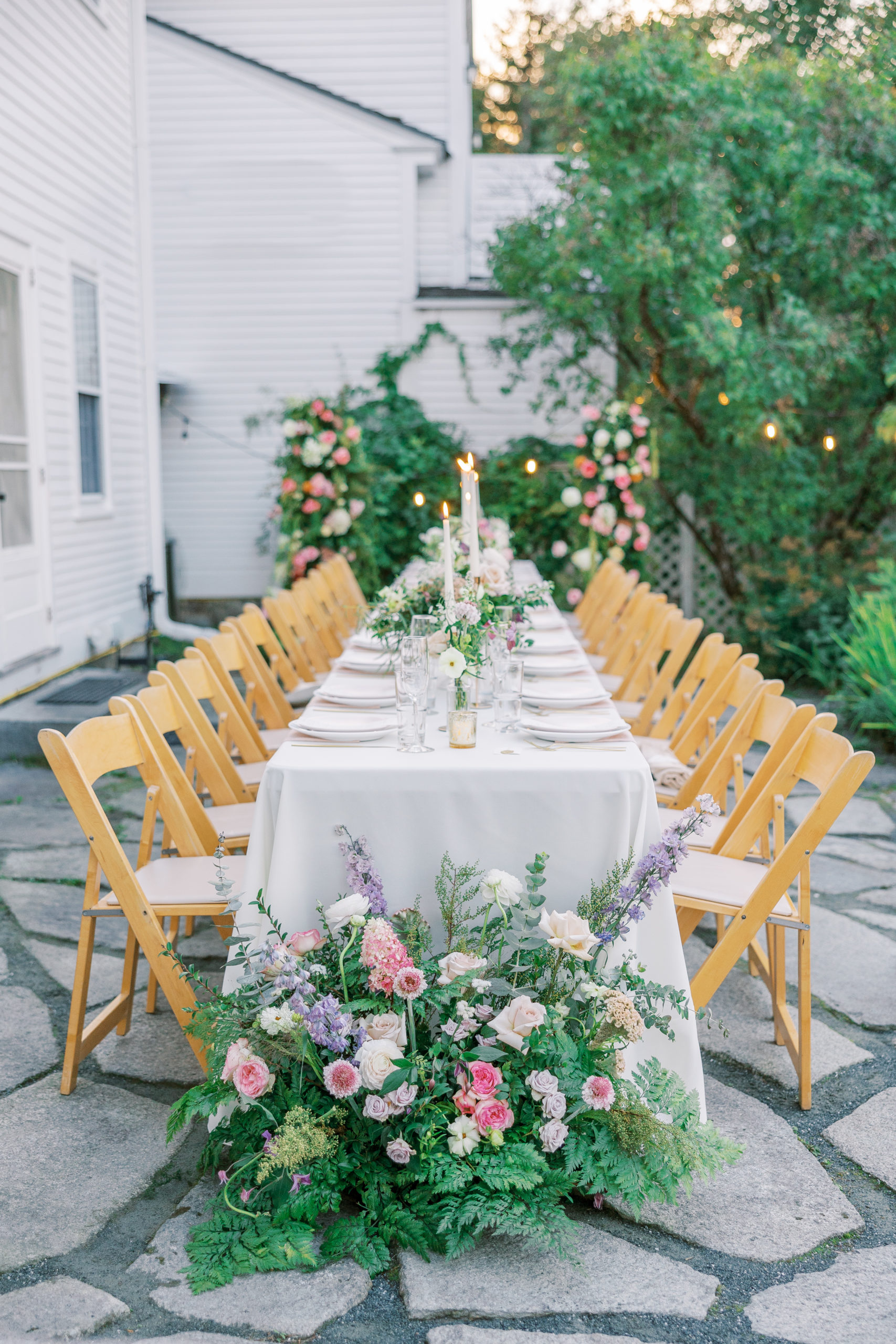 Reception table seating with one long table, tall candles, and flower centerpieces on stone patio 
