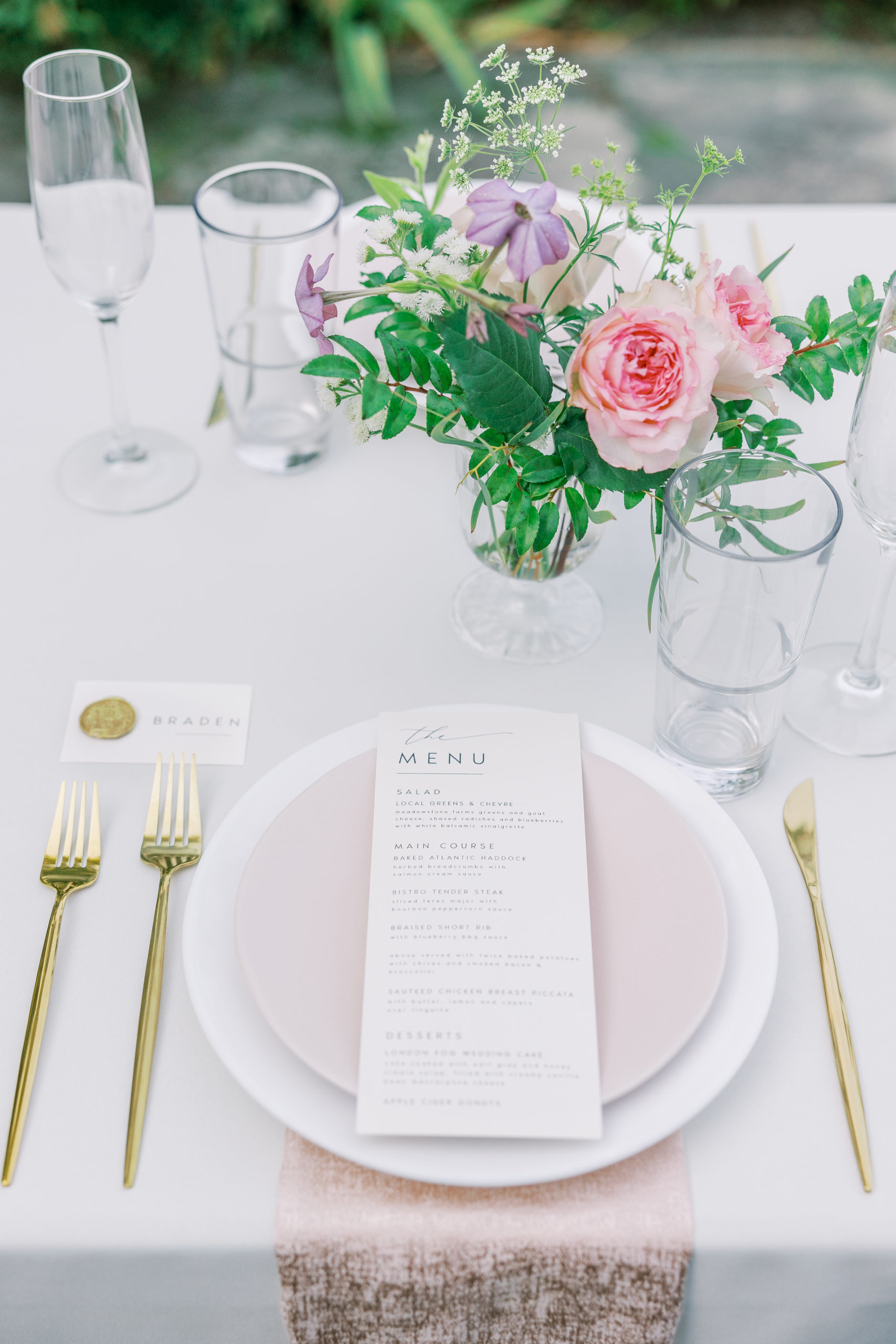 Reception table with menu, gold utensils and pink and purple flowers 