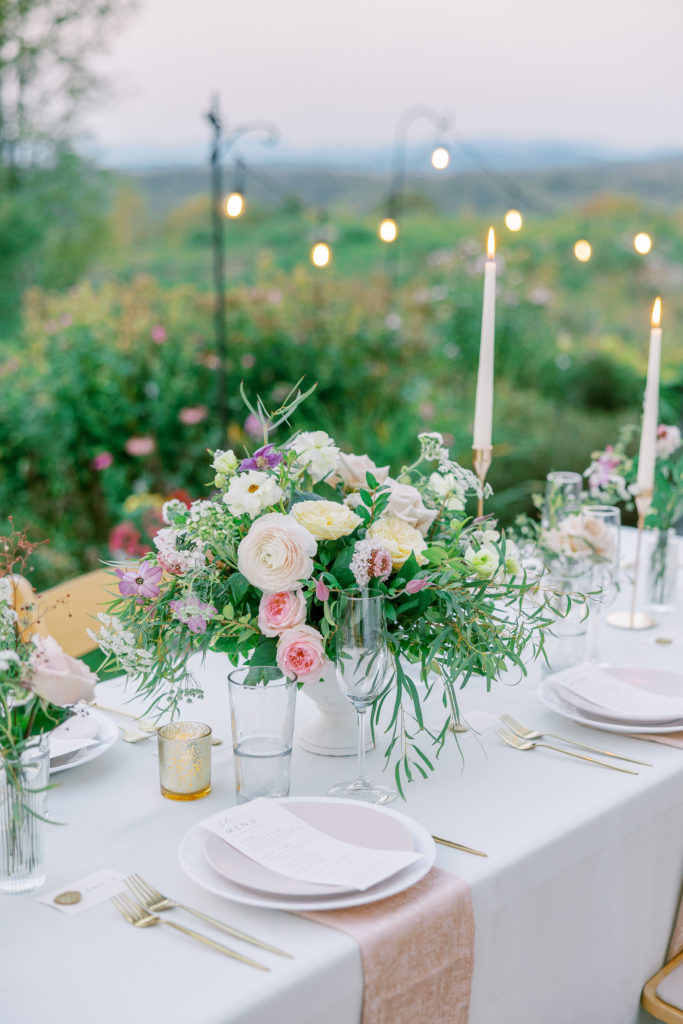 Reception table with rose centerpieces and gold and pink details overlooking the green hills 