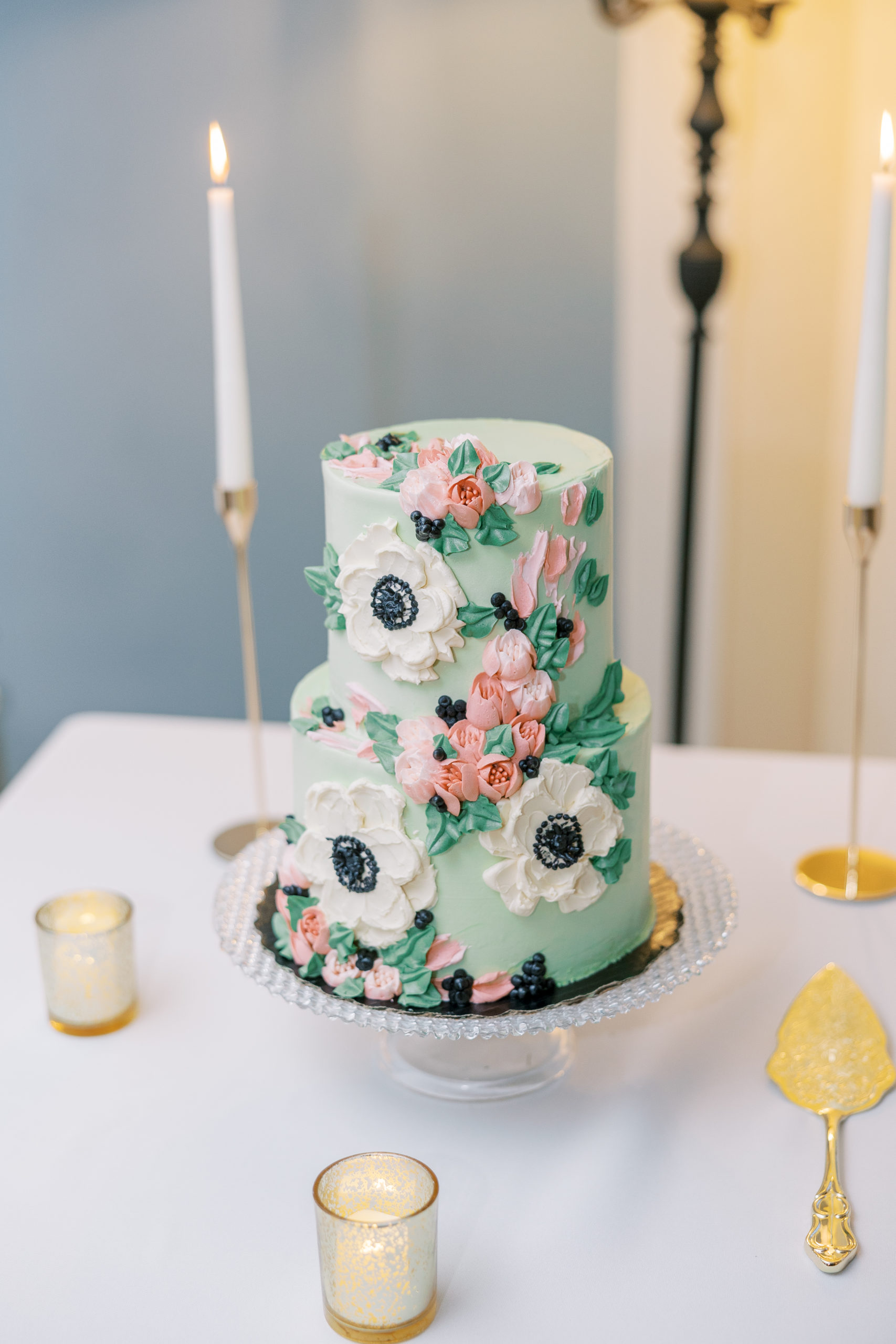 Green 2-tiered wedding cake with cream and pink flowers made of icing with gold candle holders and cake knife 