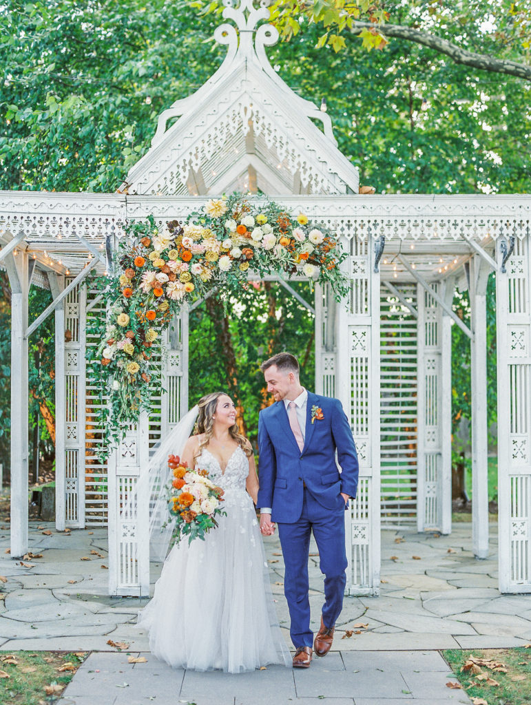 Bride and groom smile and hold hands under white antique pavilion for Terrain Glen Mills Wedding 