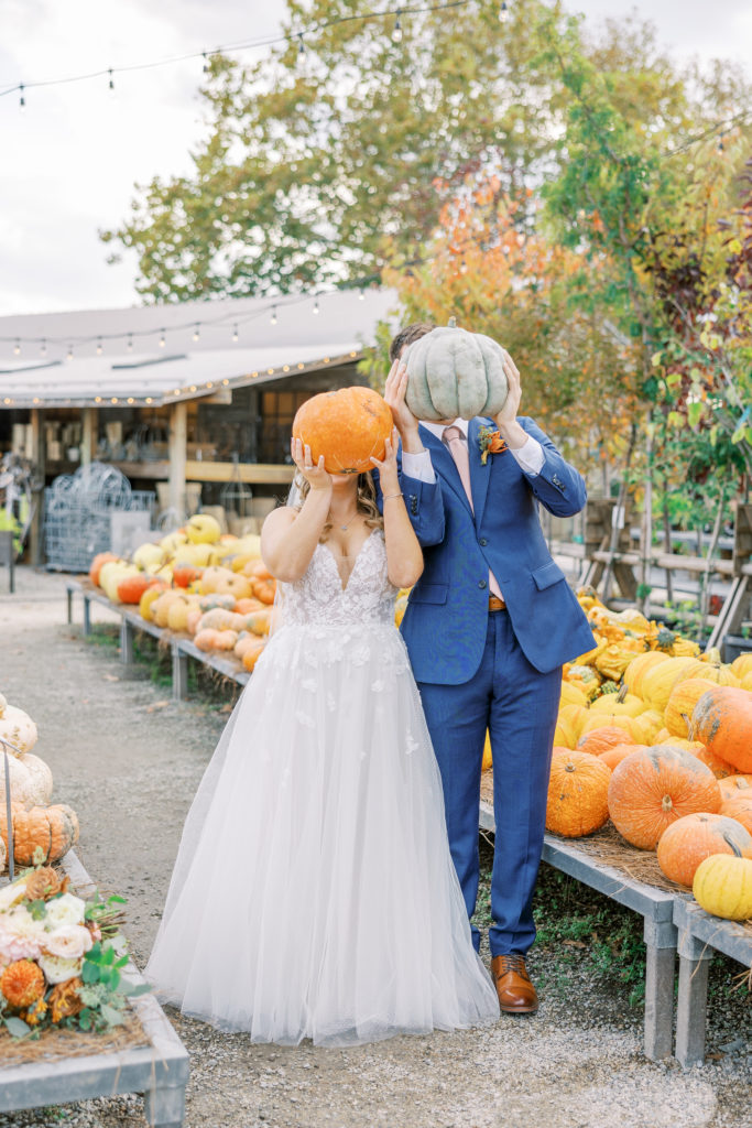 Bride and groom hold up pumpkins to their heads and pose for Terrain Glen Mills Wedding