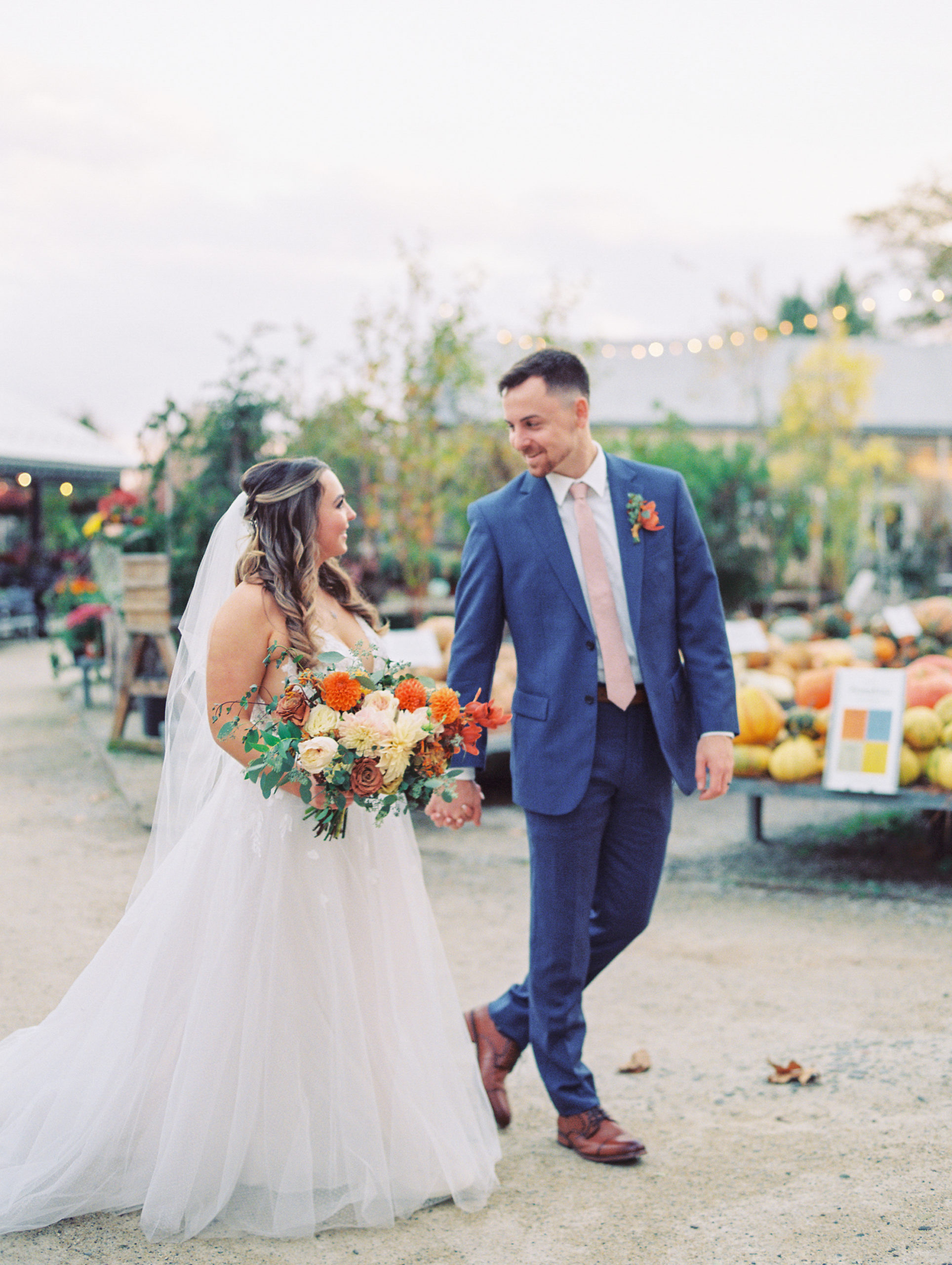 Bride and groom hold hands and smile in terrain gardens surrounded by greenery and pumpkins for Terrain Glen Mills Wedding