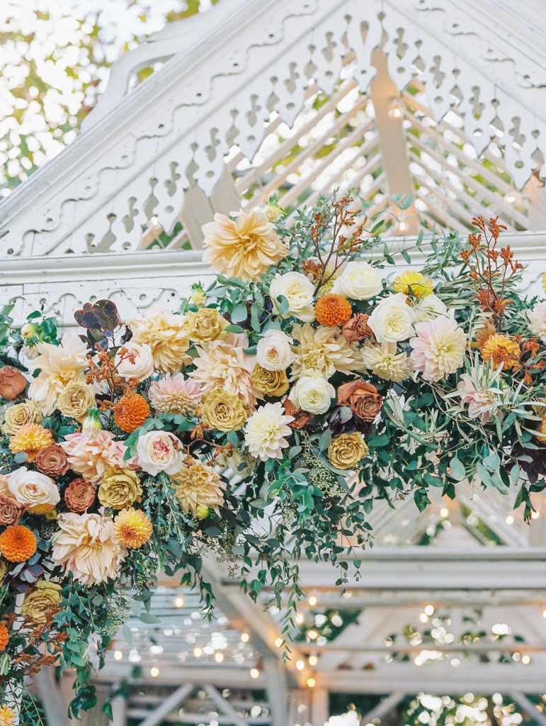 View of white pavilion and cream, orange, yellow, and pink flowers along arch for Terrain at Styer's Wedding