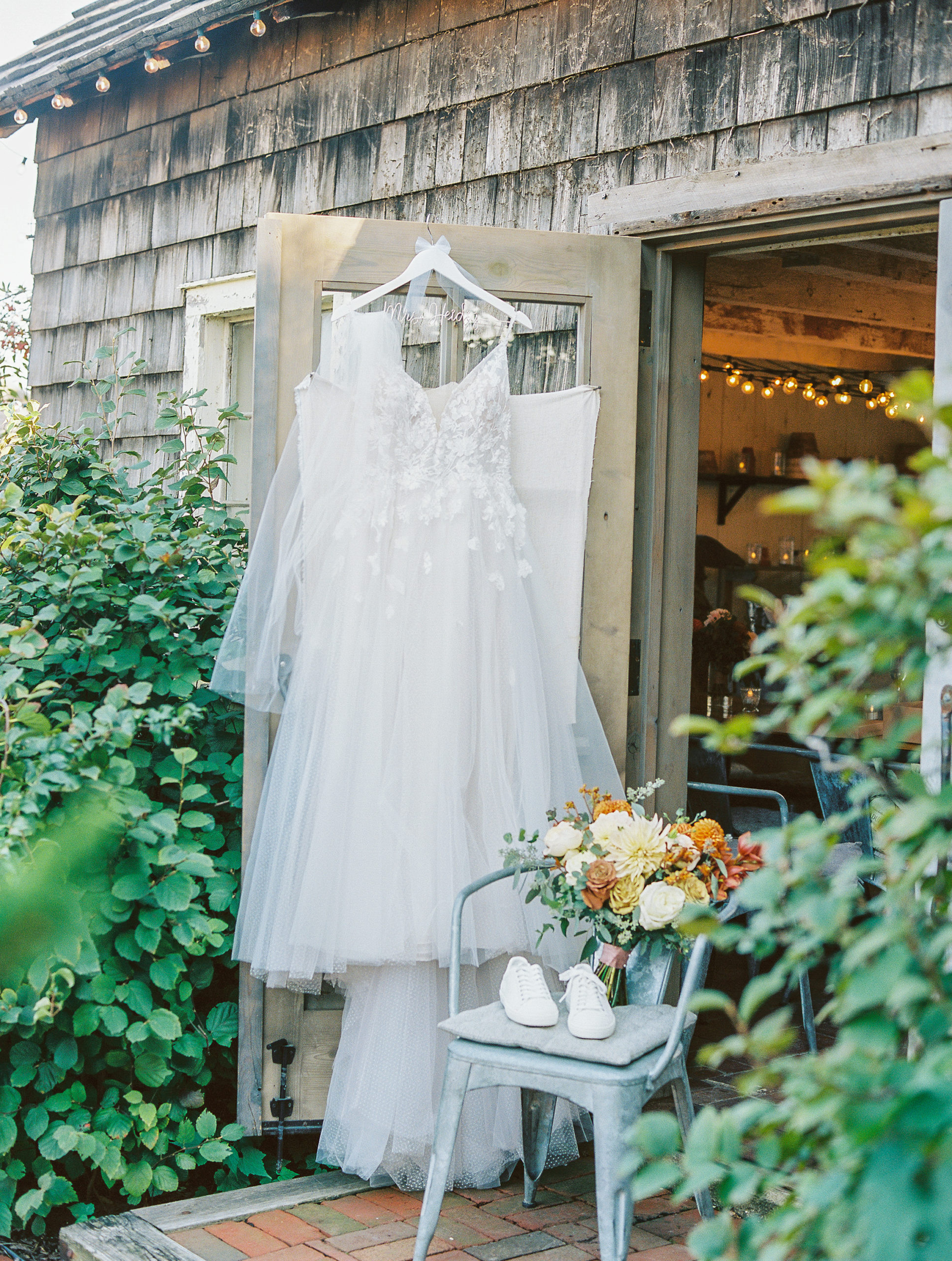 Wedding dress hung up over rustic door with autumnal bouquet and white sneakers for Terrain Glen Mills Wedding