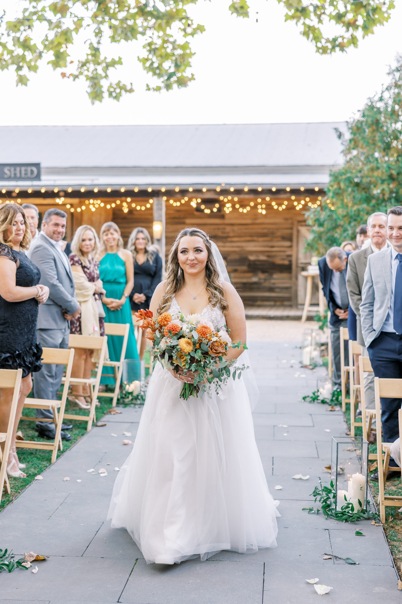Bride walks down stone path aisle holding wedding bouquet for Terrain at Styer's Wedding