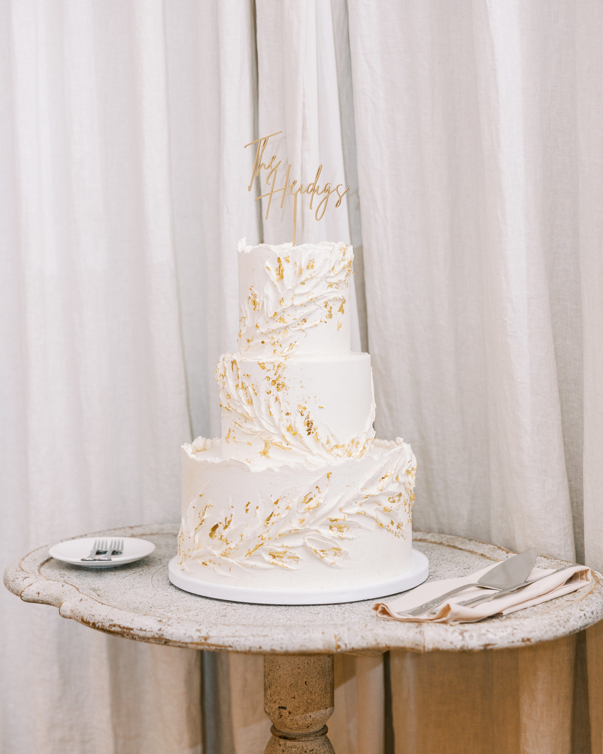 3-tiered white wedding cake with golden specks resembling flowers on top of rustic stone round table 