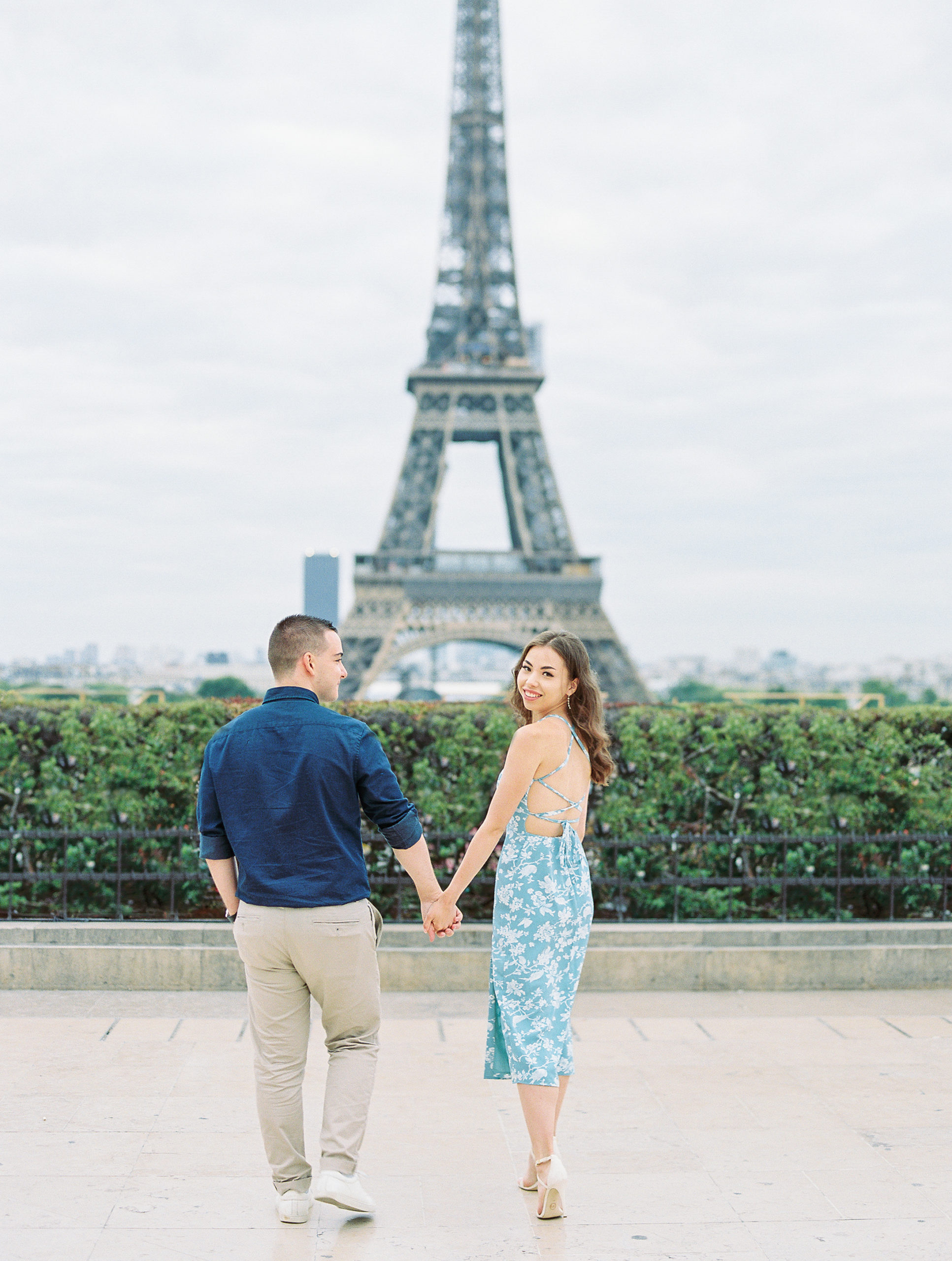 Couple holds hands and walks towards Eiffel Tower for Paris Film Photographer