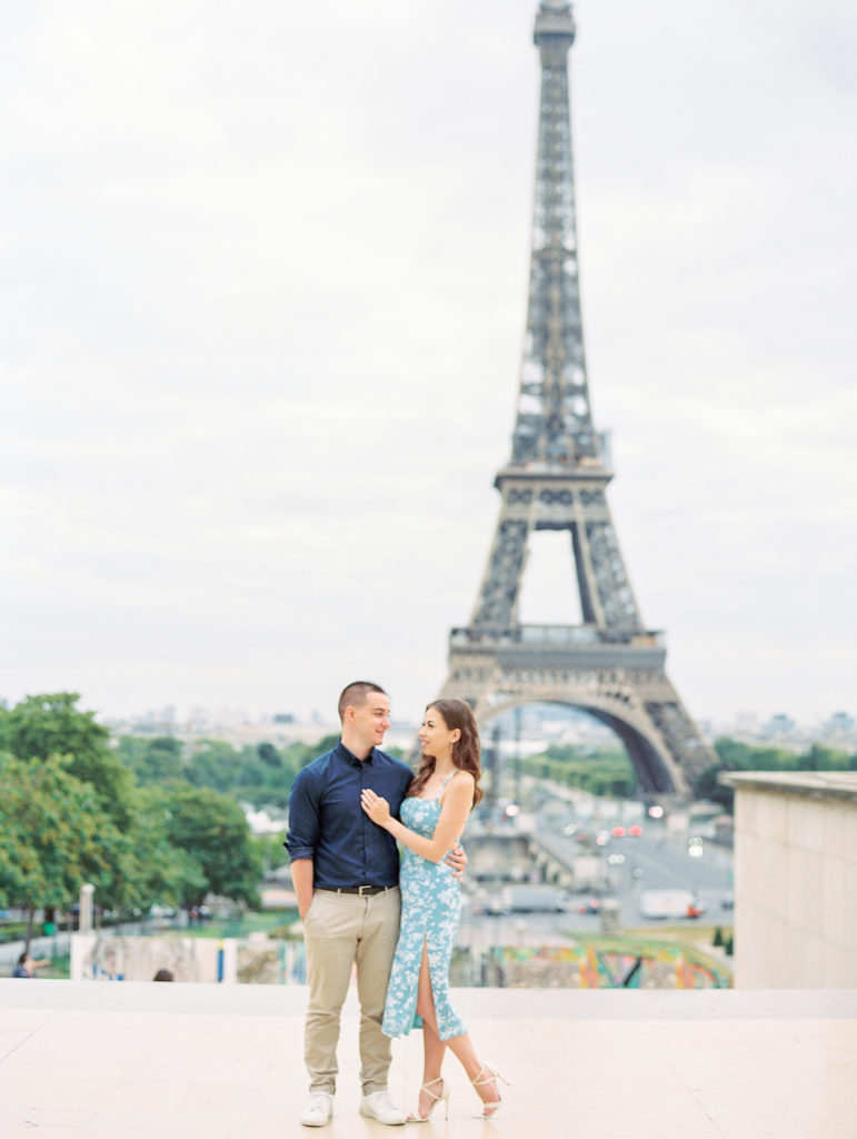 Couple embrace and smile in front of Eiffel Tower for engagement session 