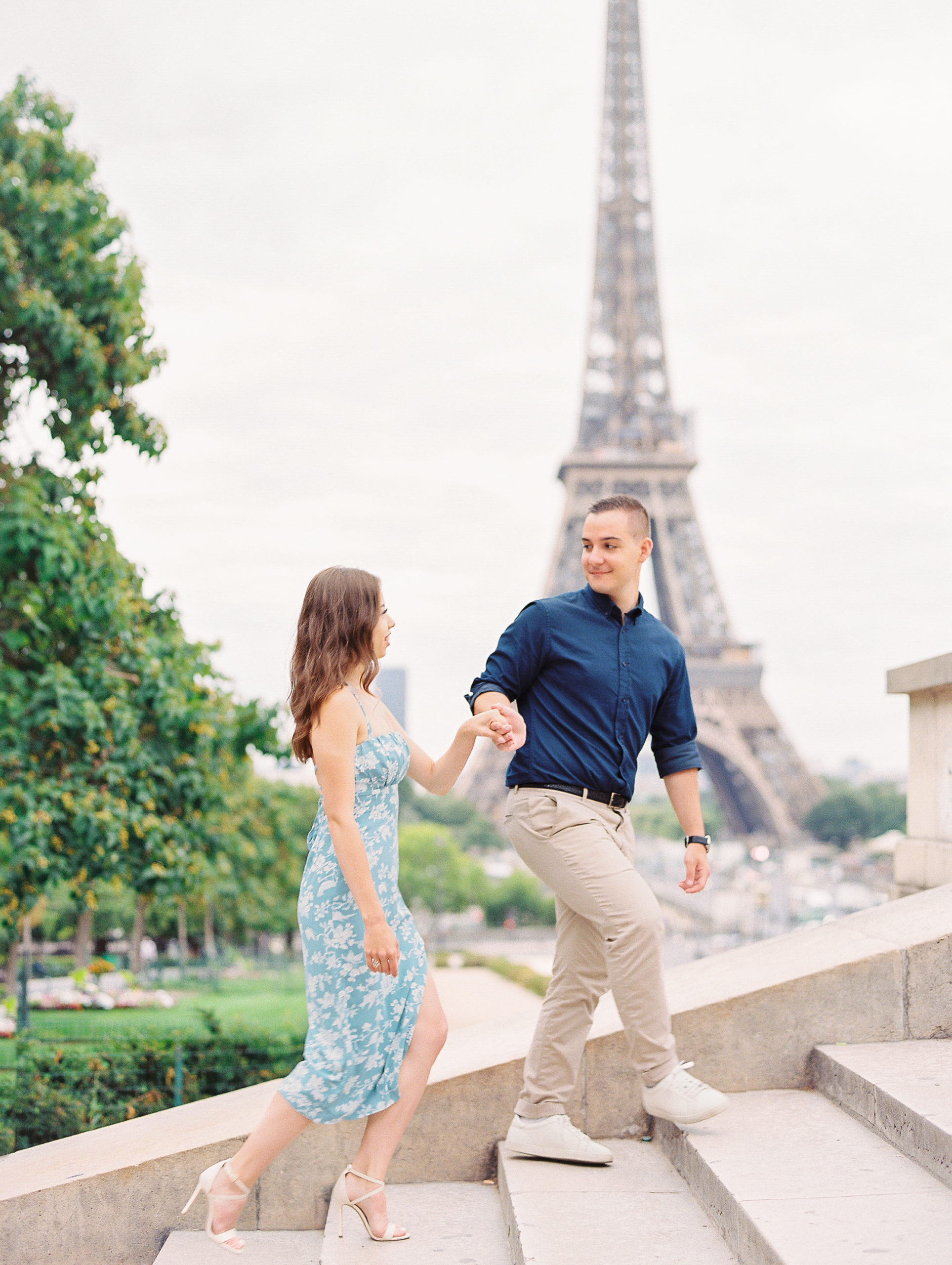 Couple walks up stone stairs with Eiffel Tower in background for Paris Engagement Session 