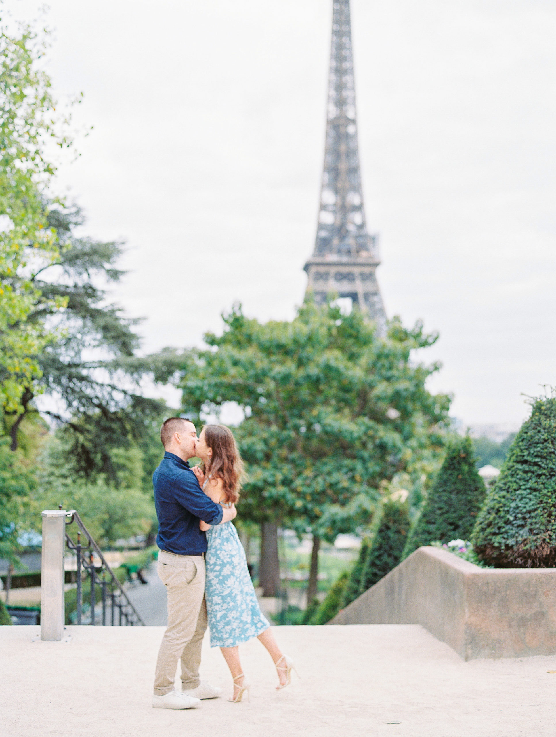 Couple embrace and share a kiss atop stairs near the Eiffel Tower for Paris Engagement Session