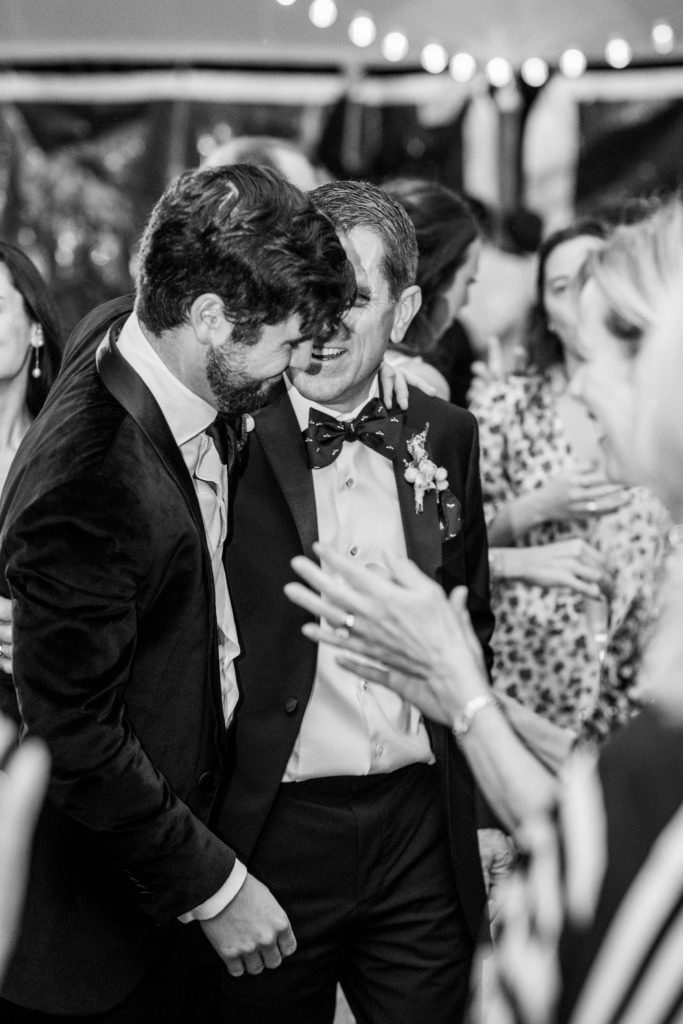 Groom and father embrace and people clap on dance floor 