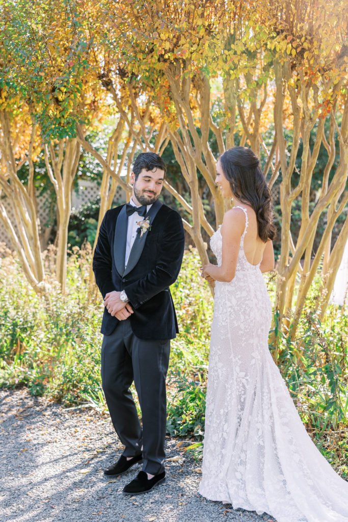 Bride and groom share a first look outside on gravel path and groom turns around 