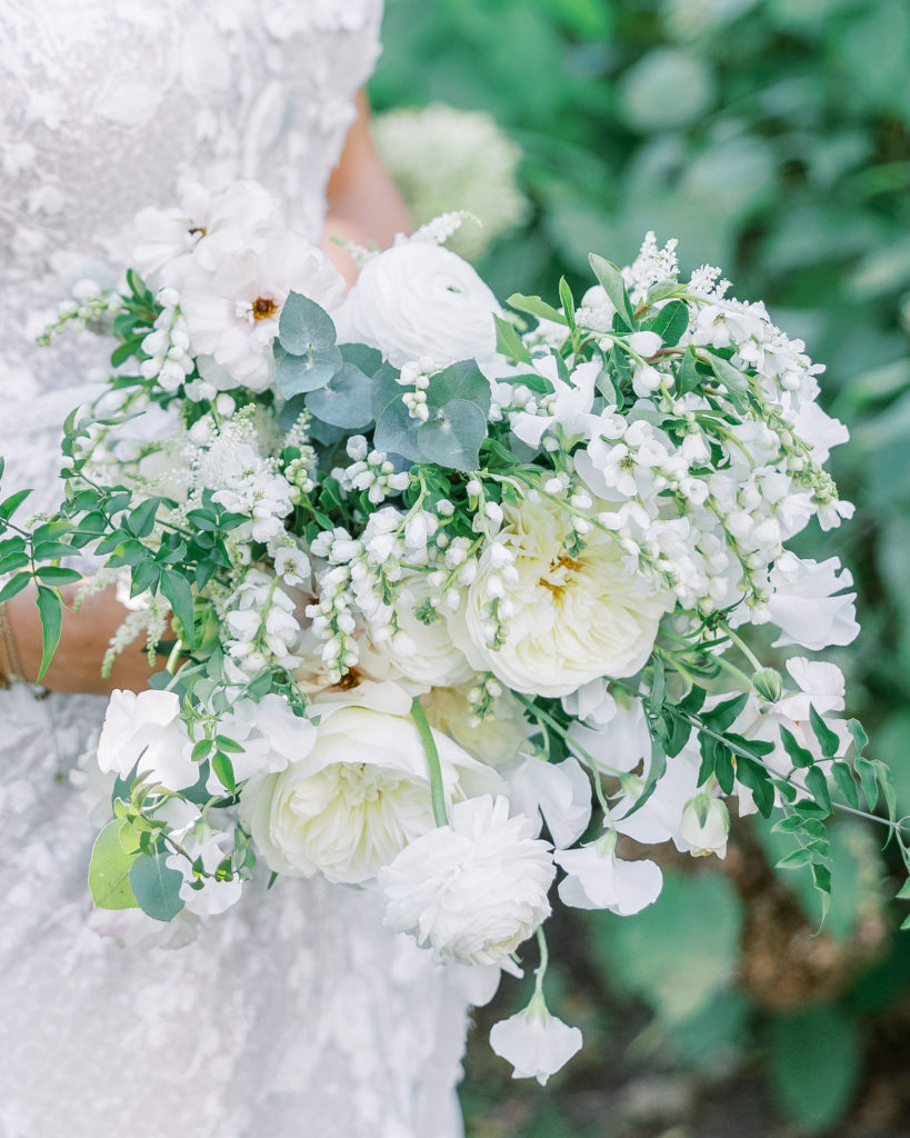 Close up of bride holding bouquet of white roses and leaves