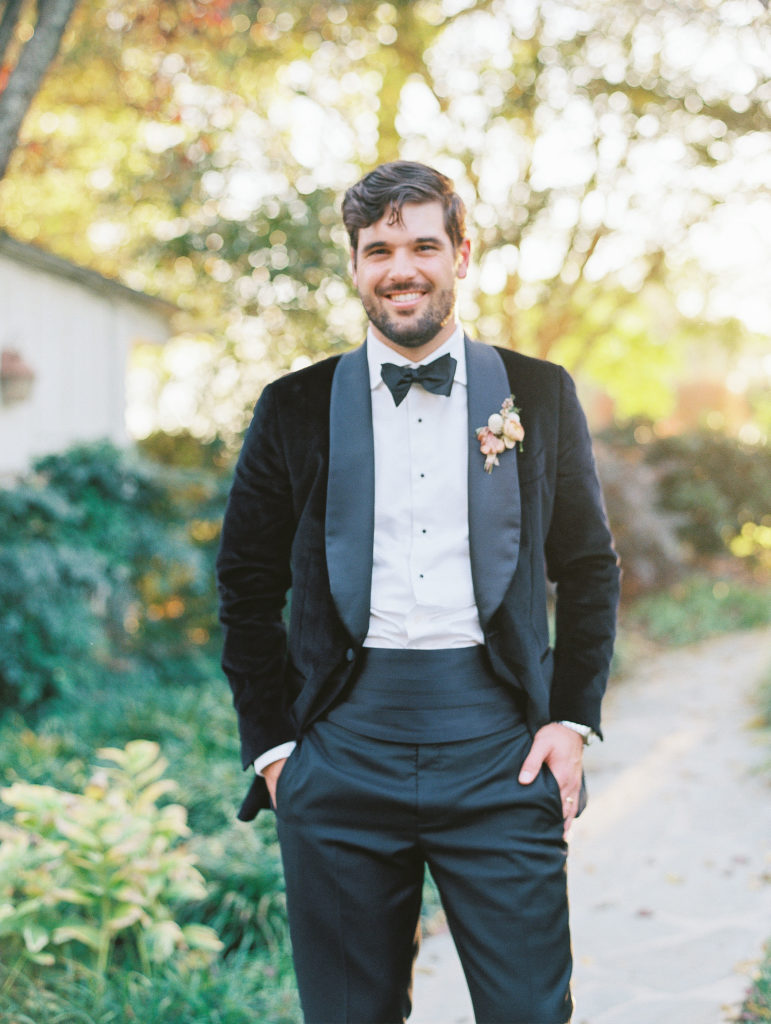 Groom smiles and poses in garden wearing black tux 