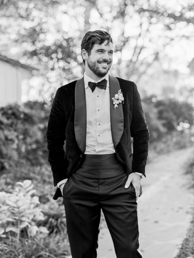 Groom poses and smiles looking away with hands in pockets in black and white for Clifton wedding photography