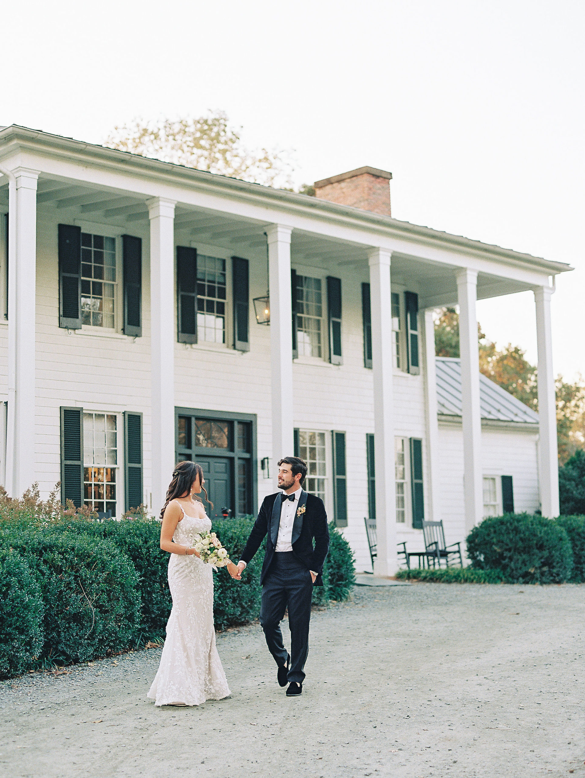 Bride and groom hold hands and in front of white house with columns and green shutter for Clifton wedding photography