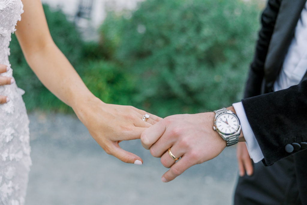 Up close view of couple holding hands with wedding rings and silver watch 