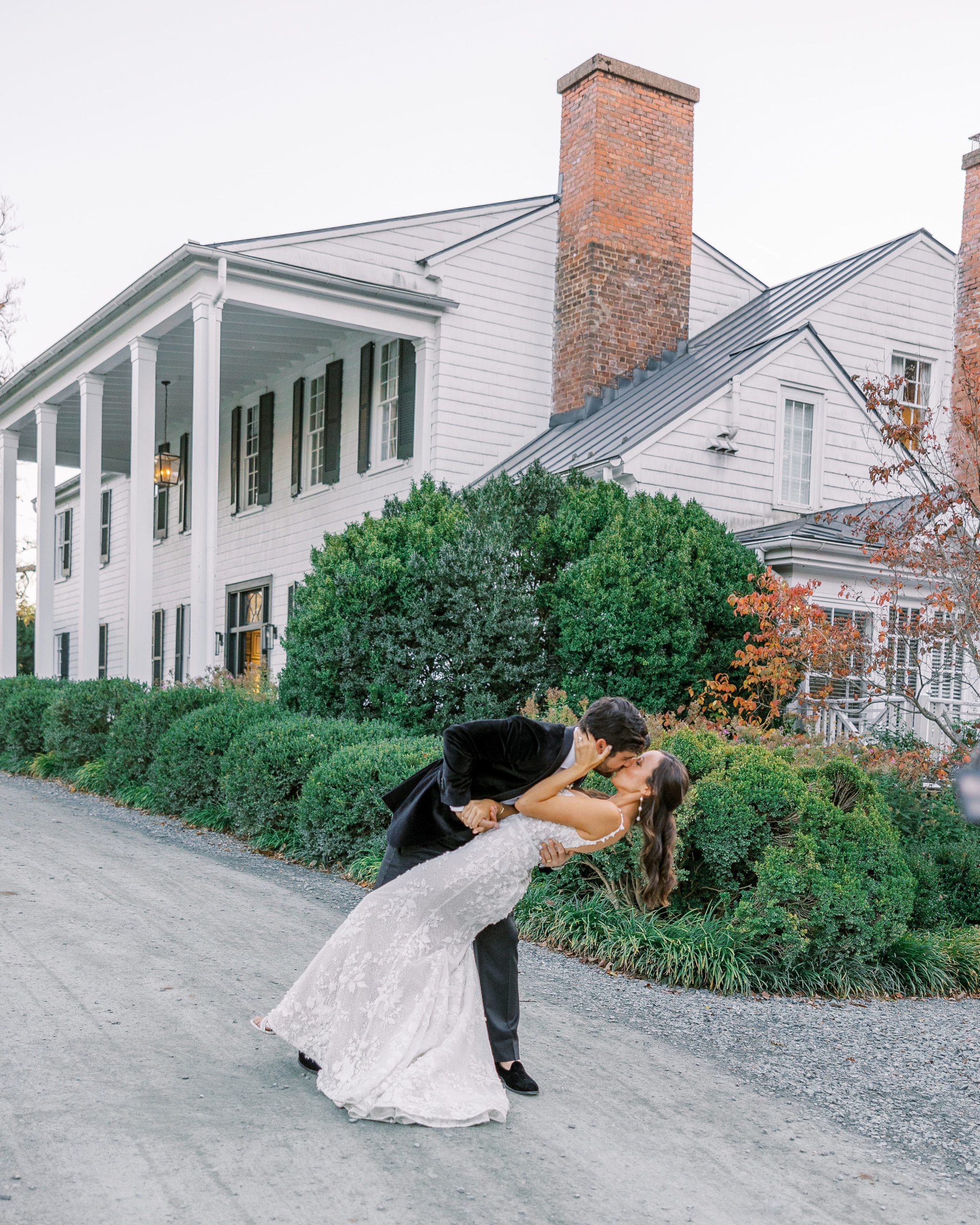 Groom dip kisses bride in front of white house on gravel pathway for Clifton wedding photography