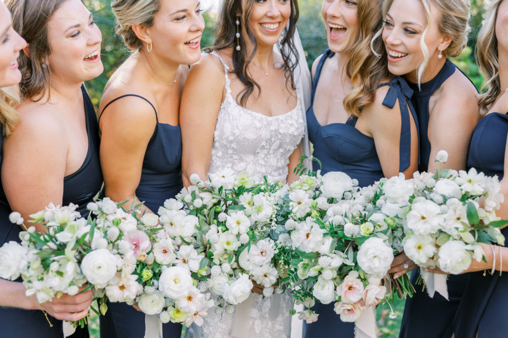 Bride and bridesmaids put bouquets together and smile wearing navy blue dresses for Clifton wedding photography